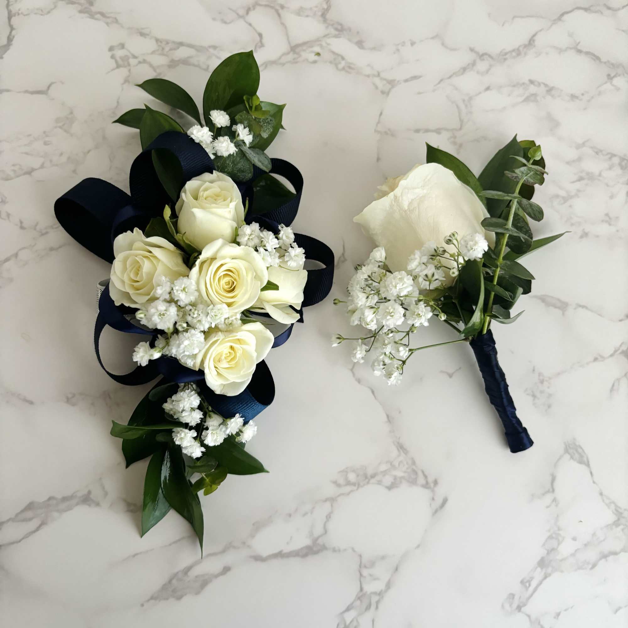 White rose bouquet and boutonniere with dark ribbon and greenery