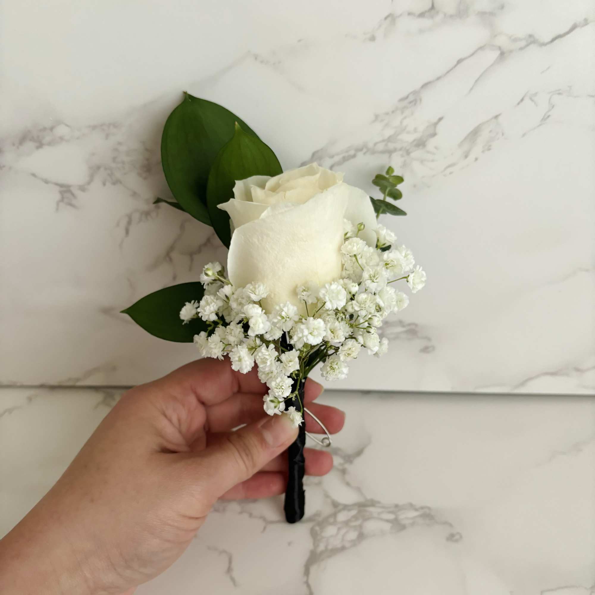 White rose boutonniere with baby's breath and green leaves