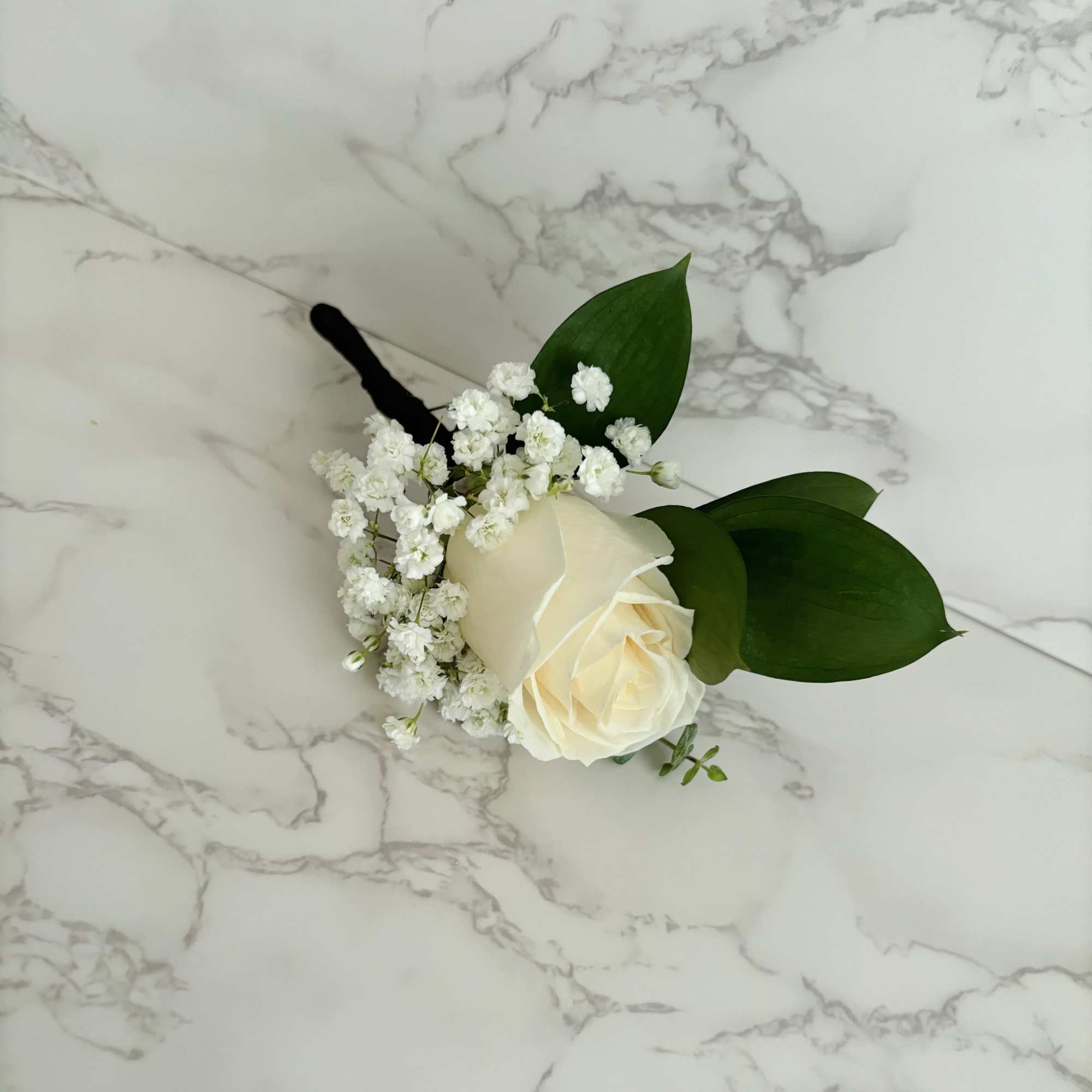 White rose boutonniere with baby's breath and green leaves