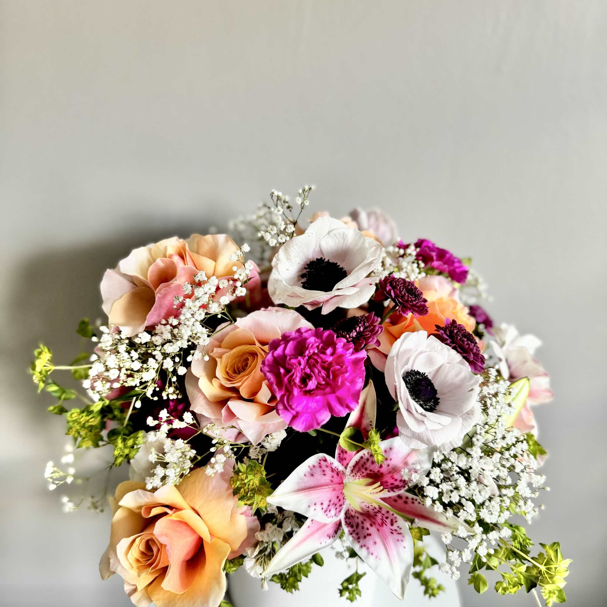 Mixed arrangement of peach roses, white lilies, and bright pink flowers in a white vase