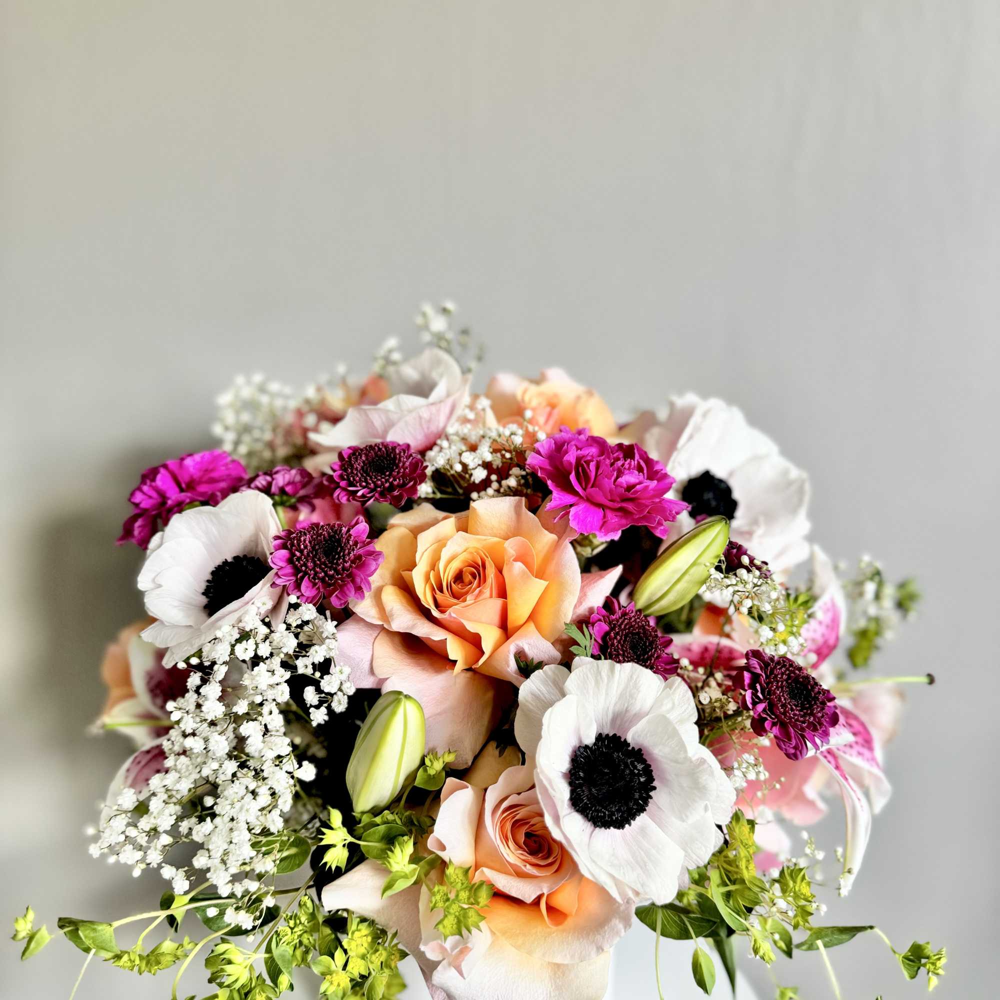 Peach roses, white anemones, and bright pink blooms arranged in a white cylinder vase