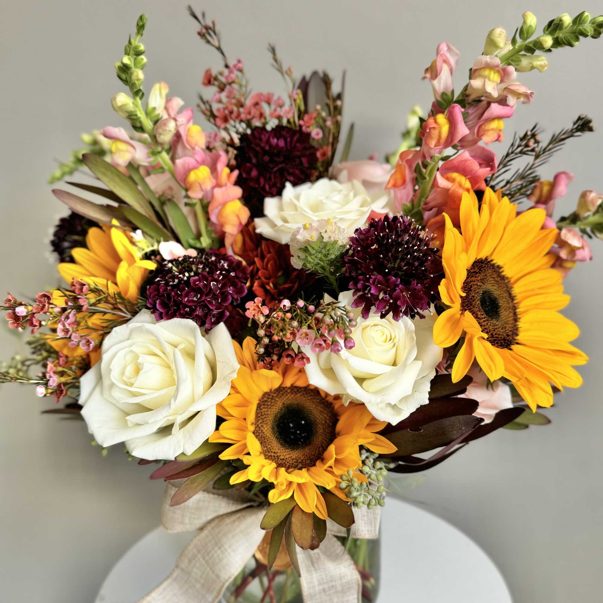 Bouquet of yellow sunflowers, white roses and pink snapdragons in a glass vase with a ribbon bow
