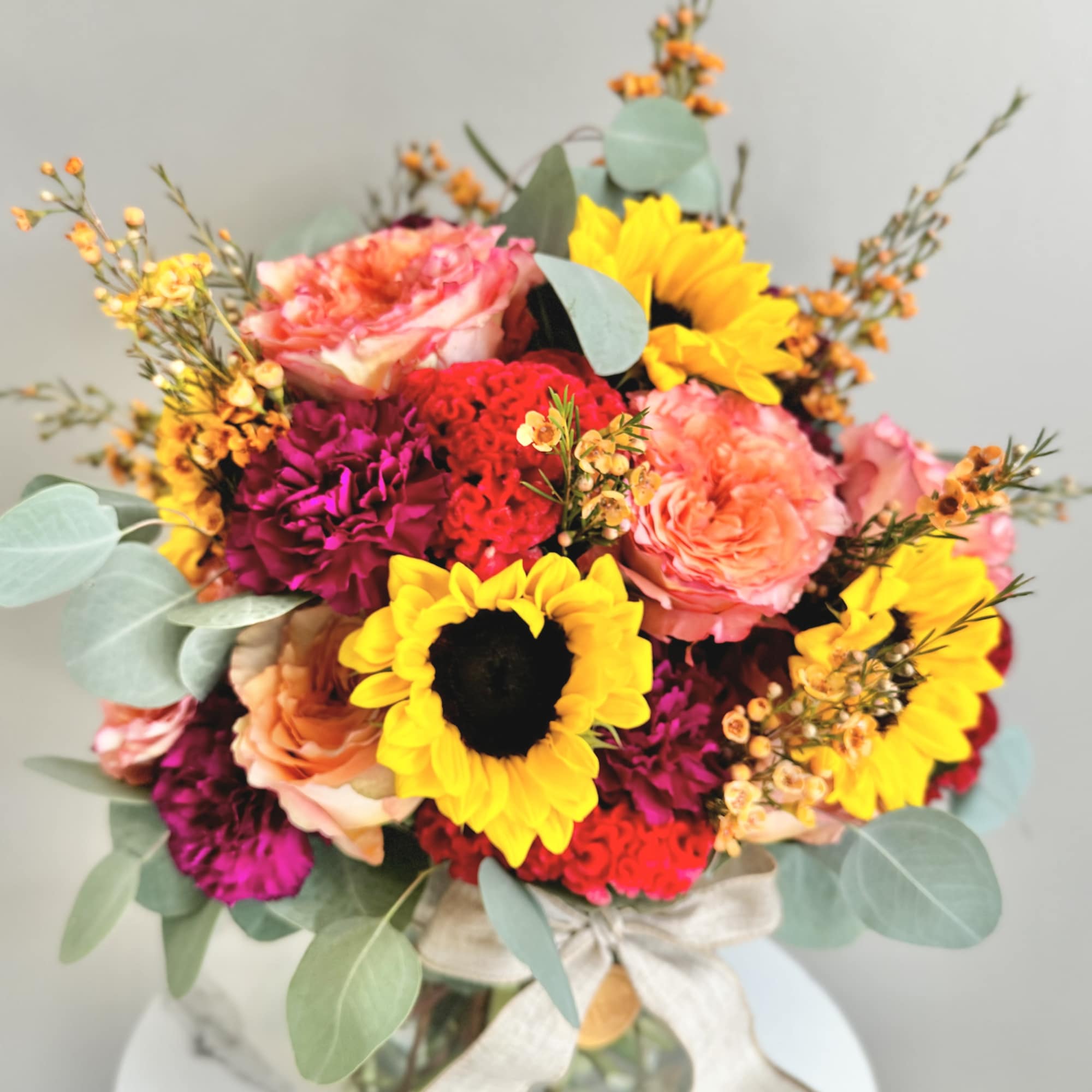 Bright bouquet of sunflowers, roses, and mixed blooms in a glass vase with a bow