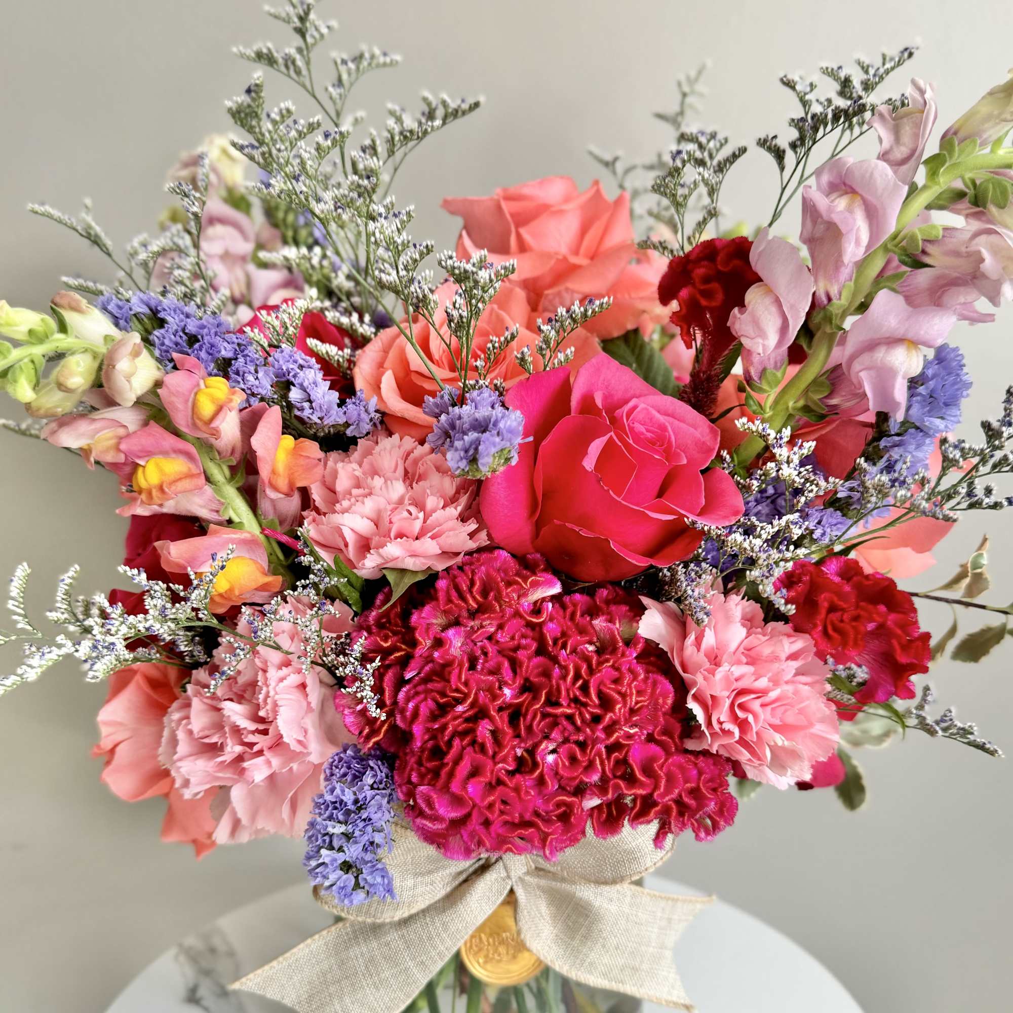 Bright mixed bouquet of pink roses, carnations, and snapdragons in a clear glass vase with a bow