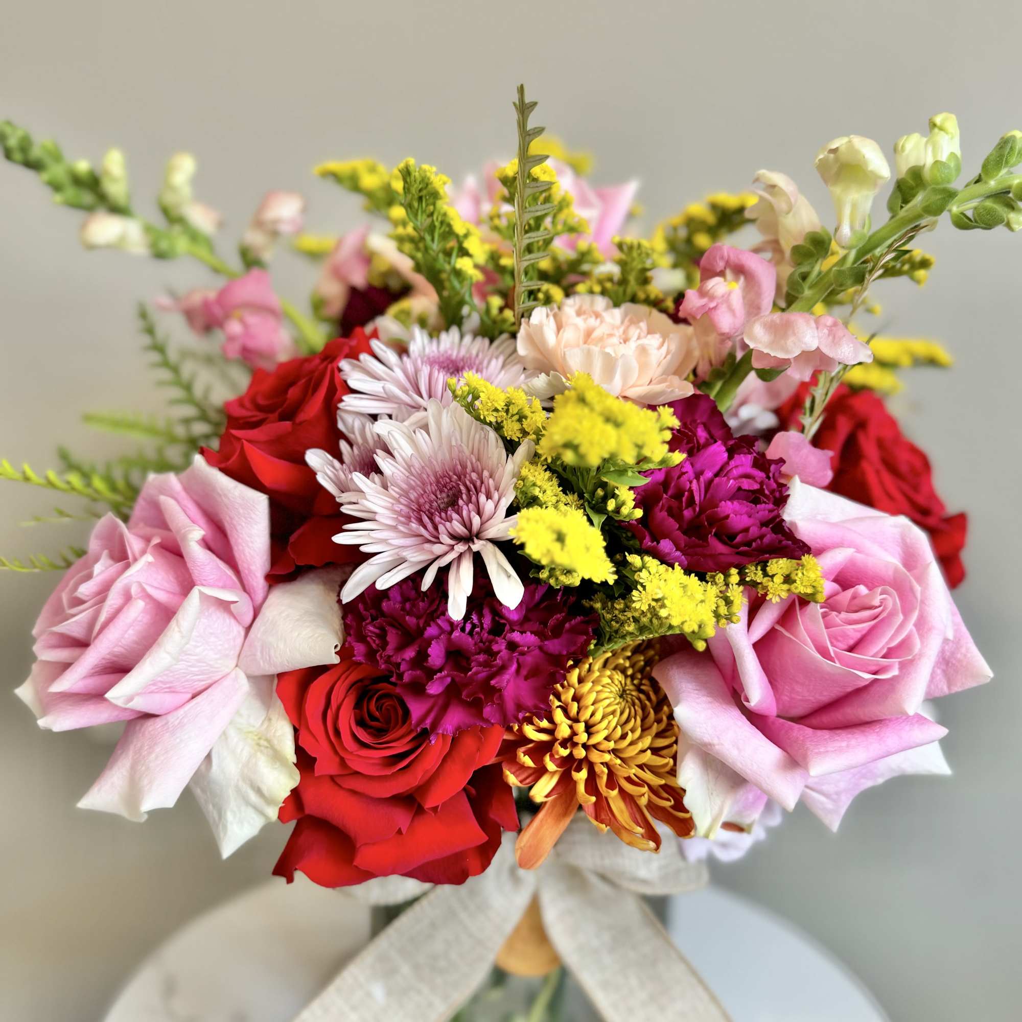 Vase arrangement of pink and red roses with mums, carnations, and snapdragons in bright mixed colors.