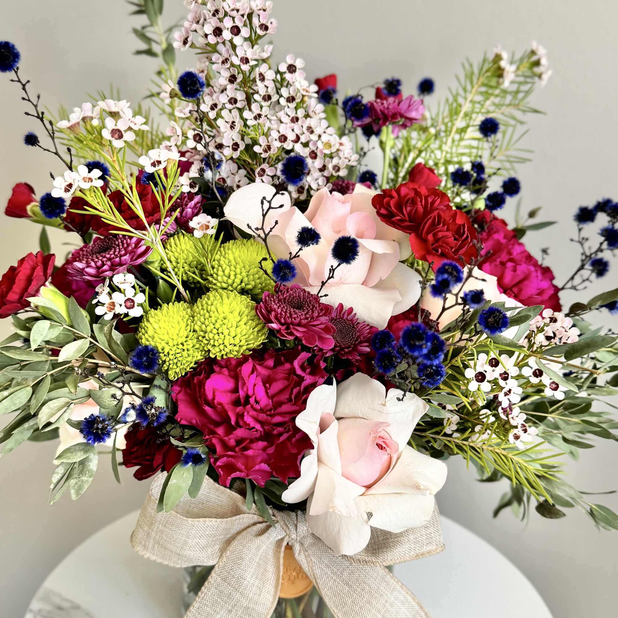 Colorful bouquet of pink roses, red blooms and green mums in a glass vase with a linen bow