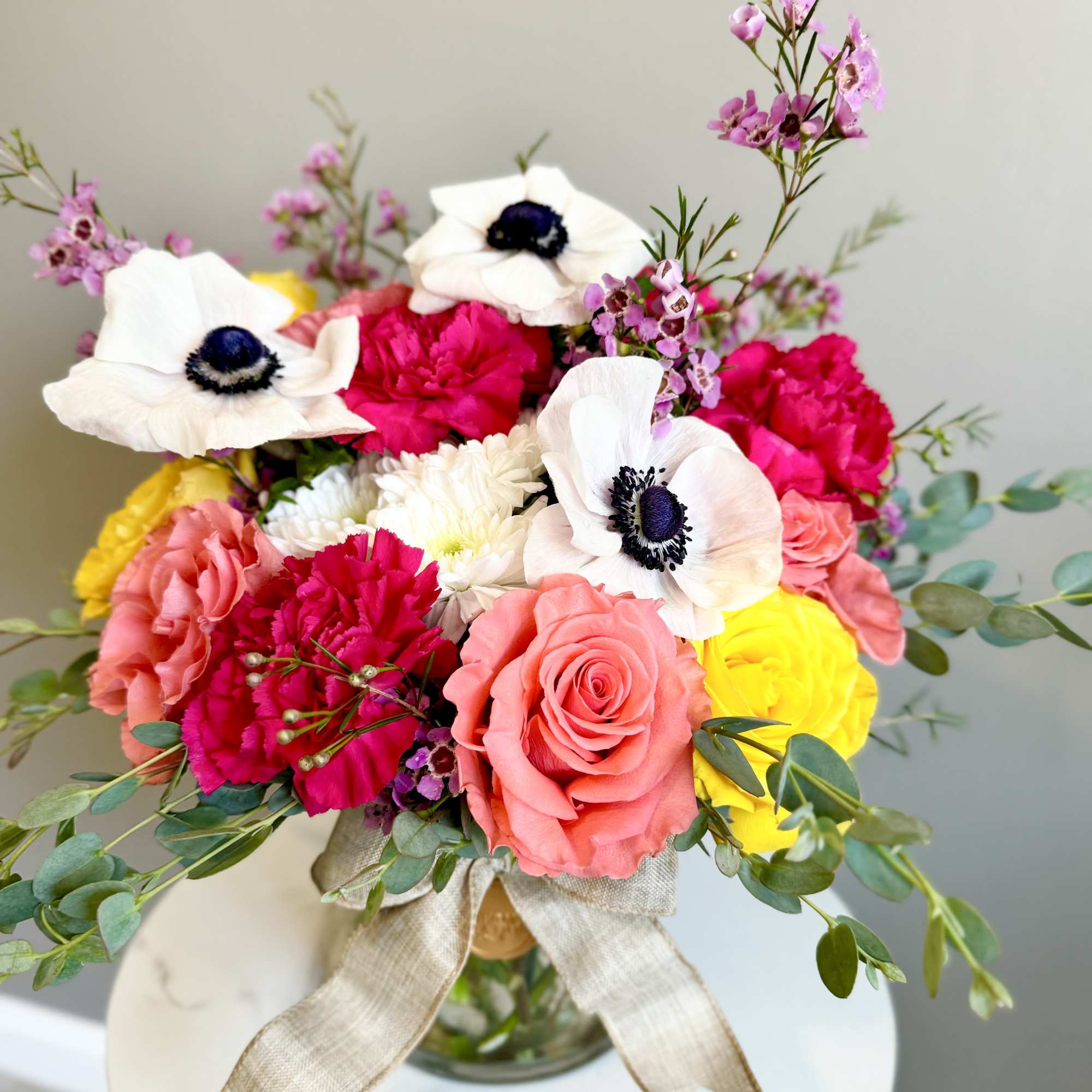 Bright mixed bouquet of coral roses, white anemones and yellow blooms in a glass vase with a ribbon bow
