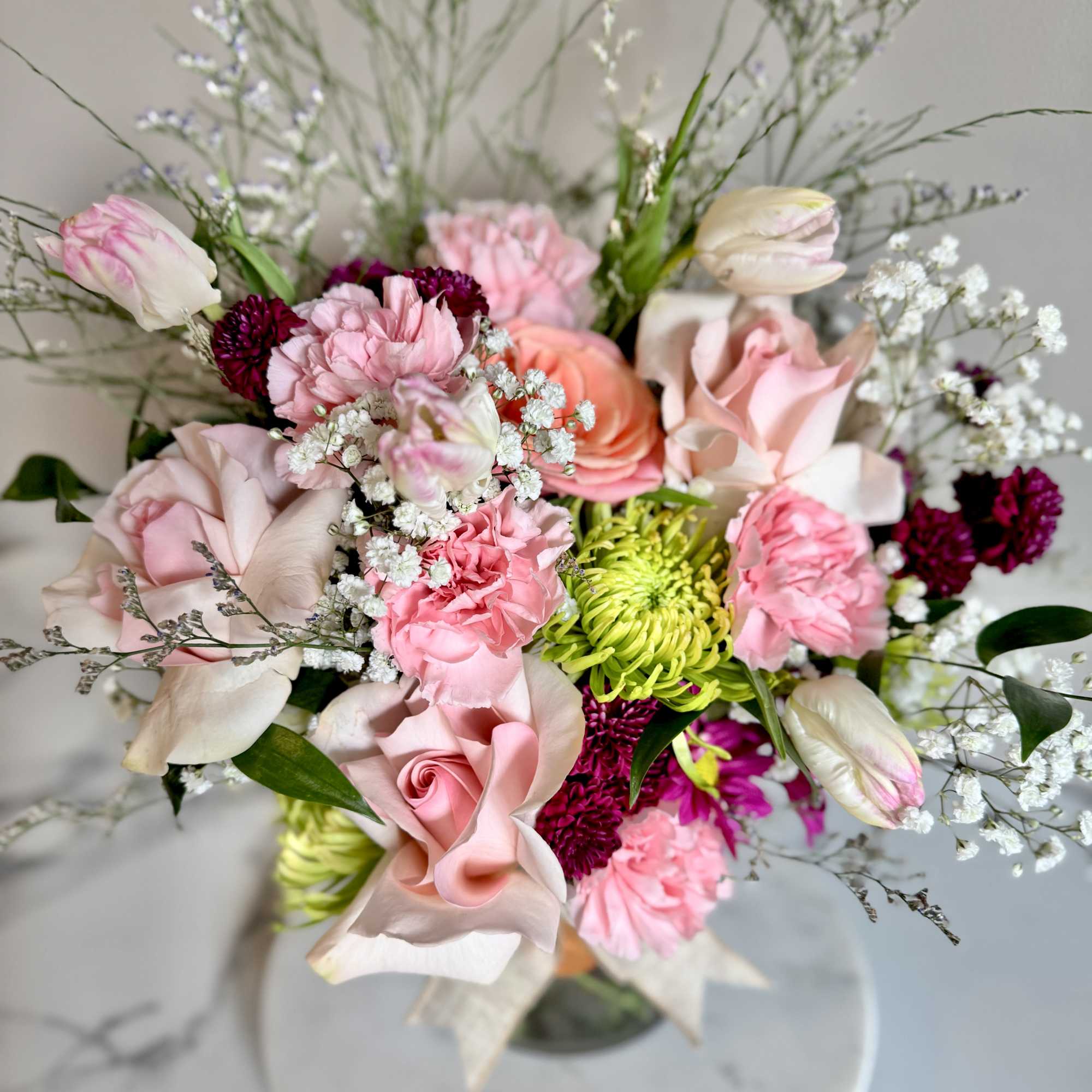 Mixed bouquet of pink roses, carnations, tulips and green mums in a clear glass vase