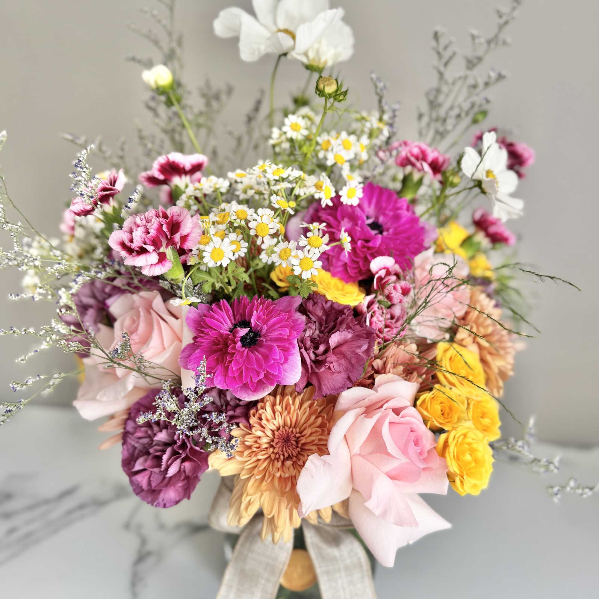 Colorful mixed bouquet of pink roses, yellow blooms, and daisies in a glass vase with a bow