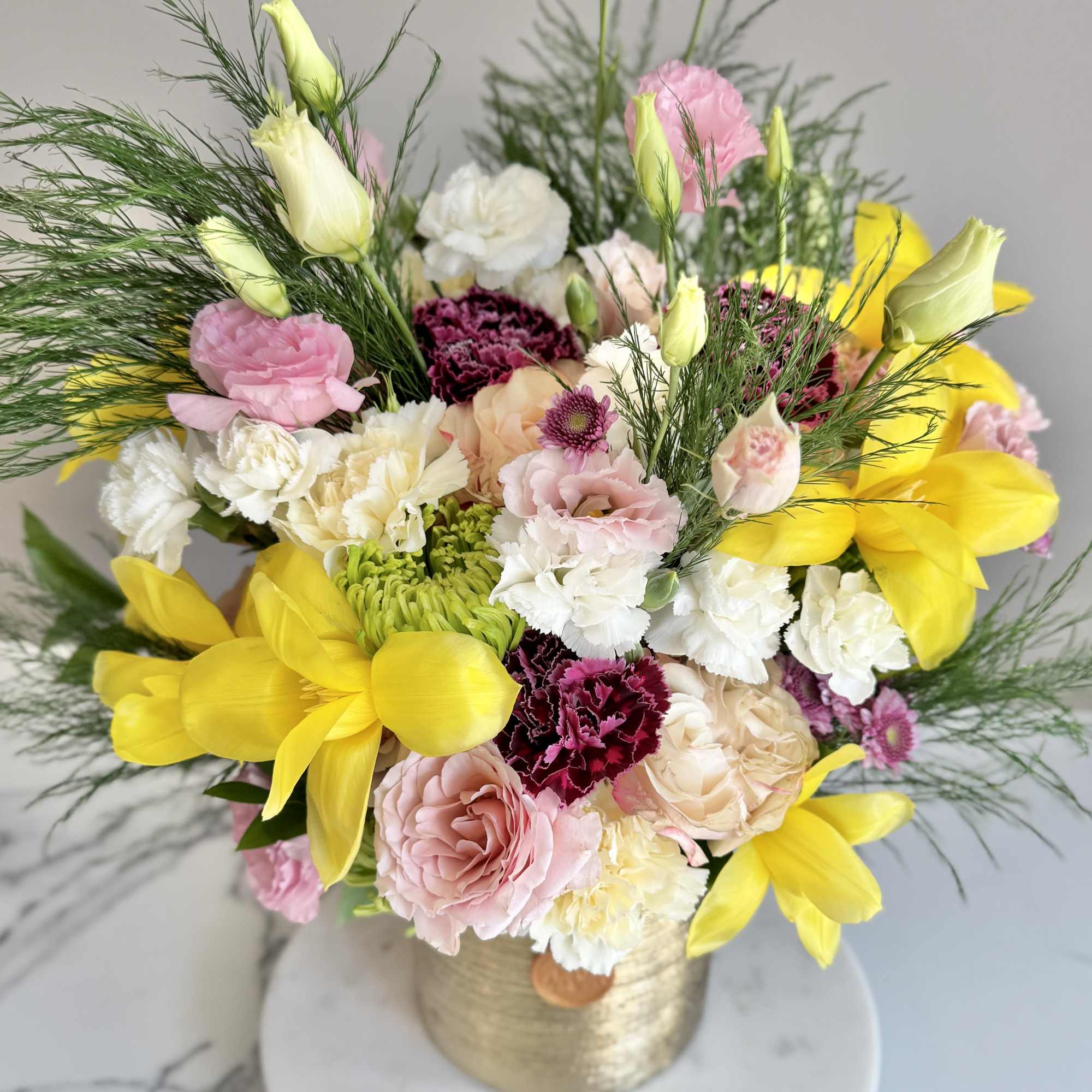 Arrangement of yellow tulips, pink roses, carnations, and white blooms in a gold vase