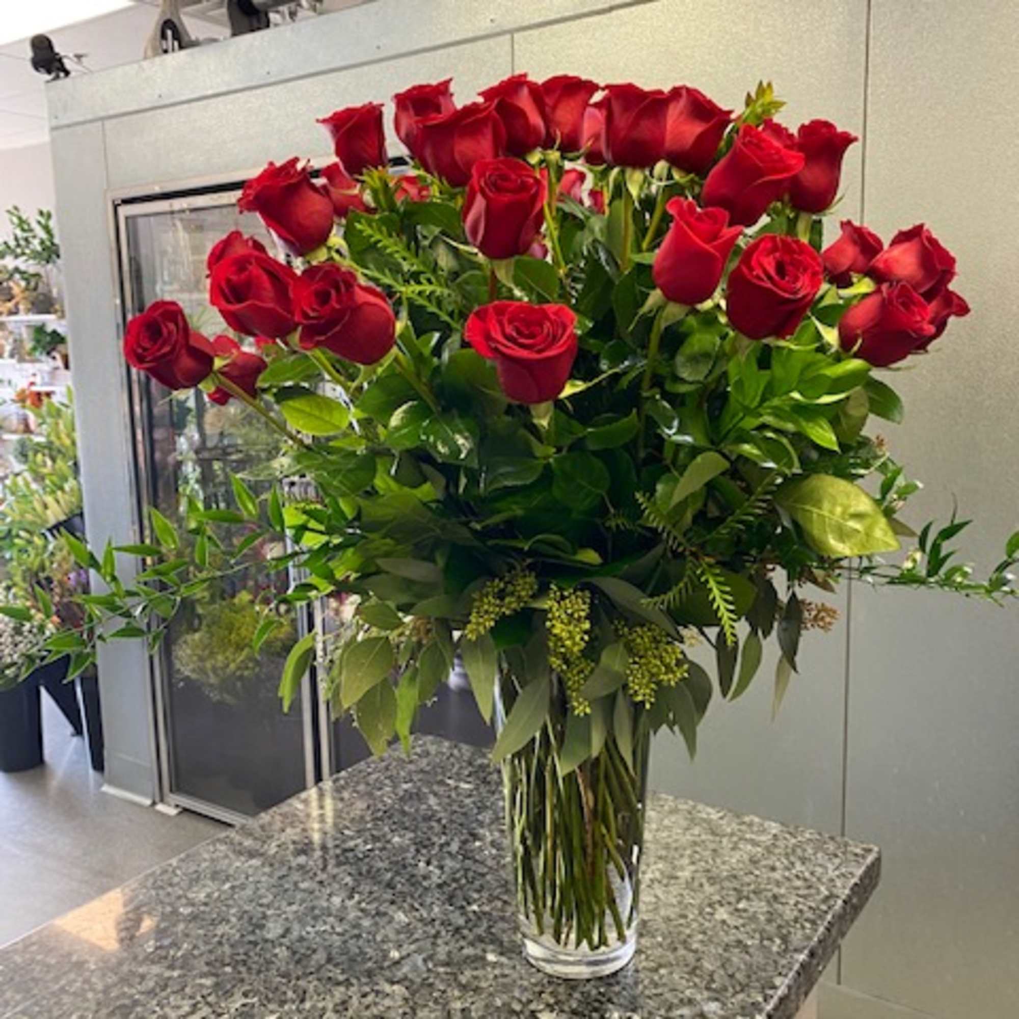 Tall vase arrangement of red roses with greenery