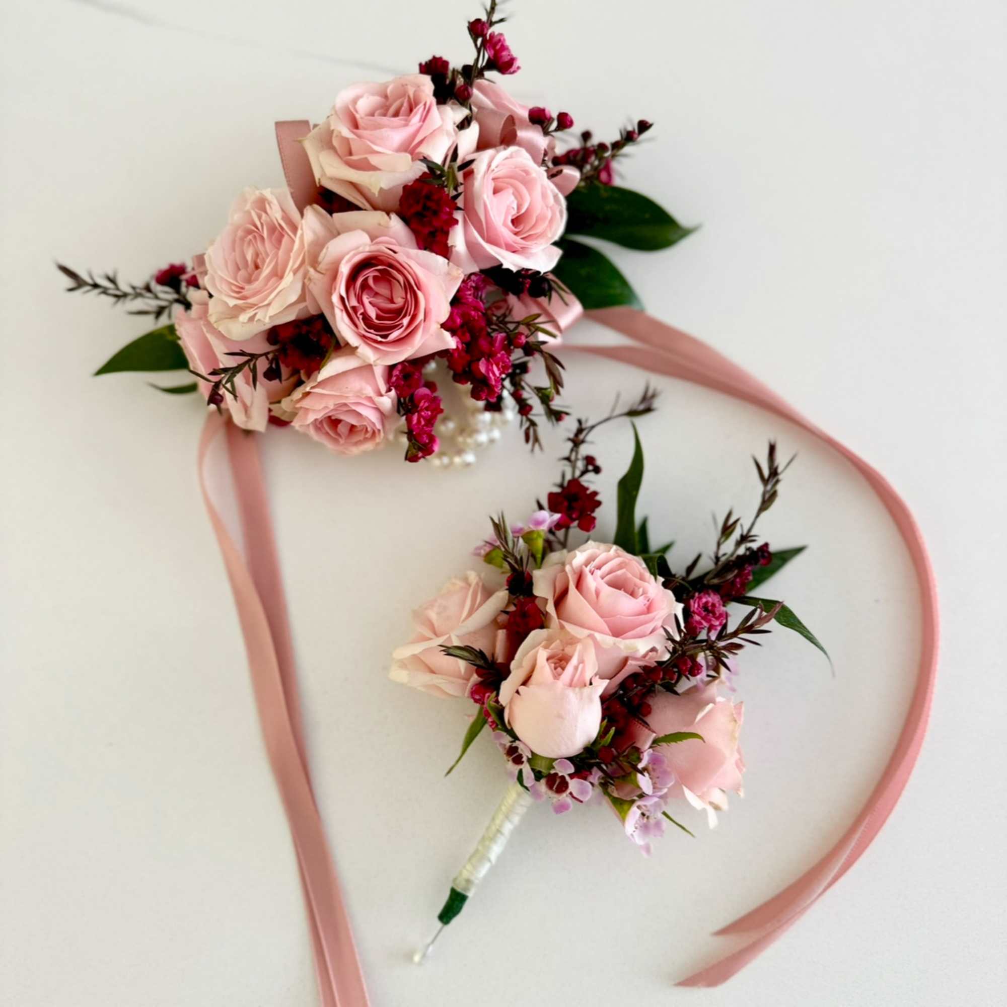 Two pink rose bouquets with ribbon streamers on a white surface
