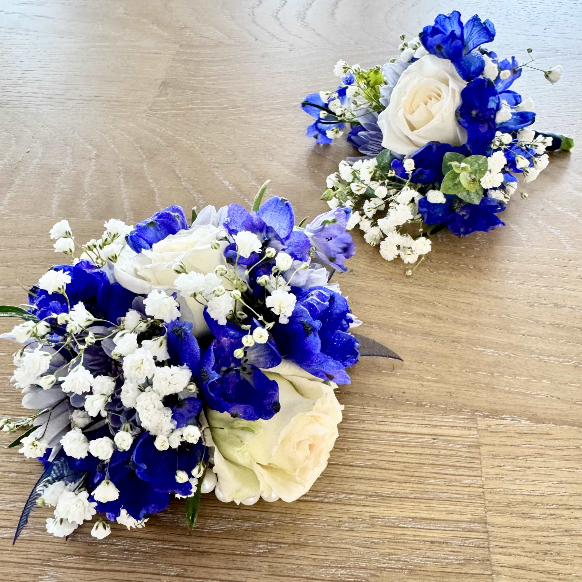 Two blue and white floral wrist corsages on a wooden surface