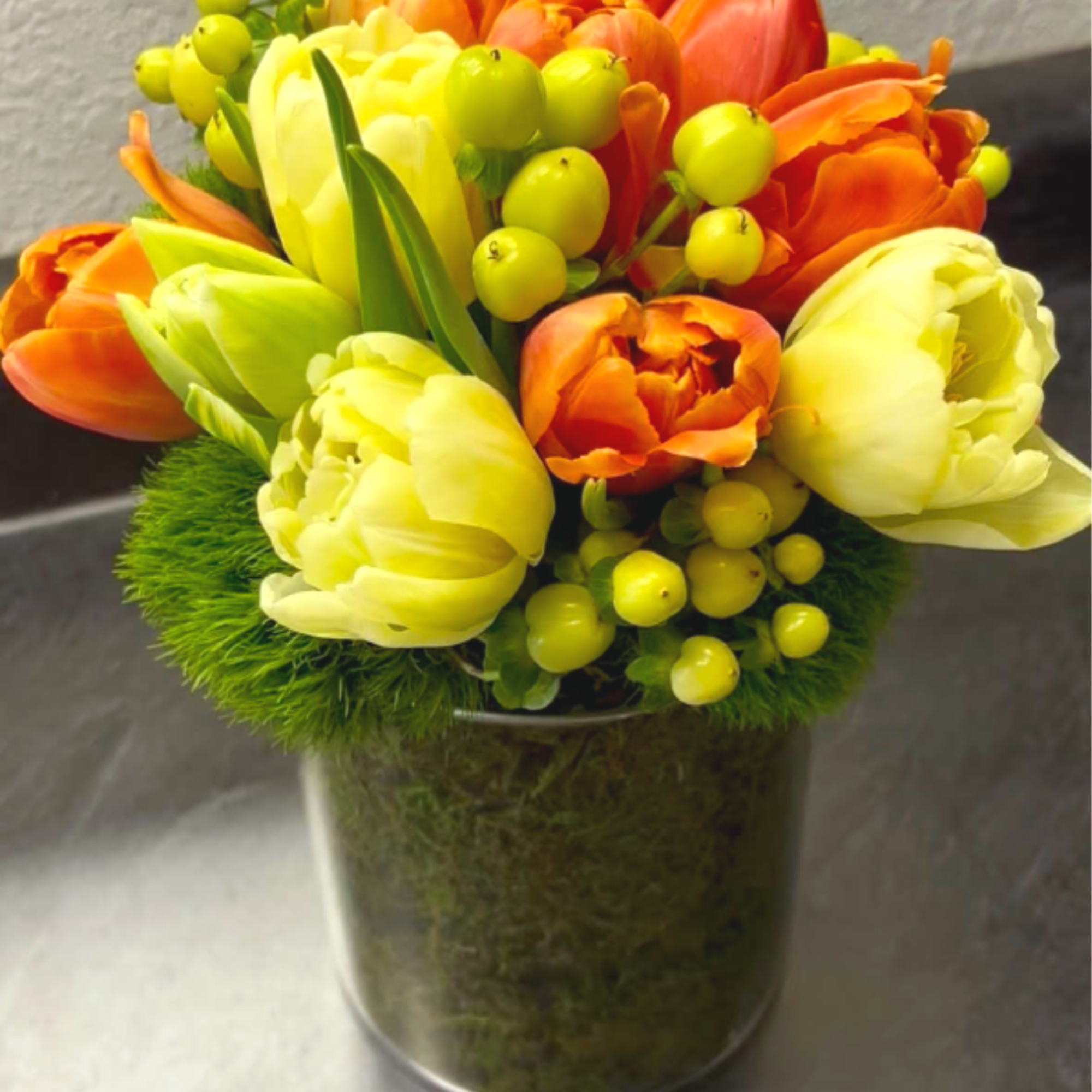Orange and yellow tulips arranged in a glass vase with green berries