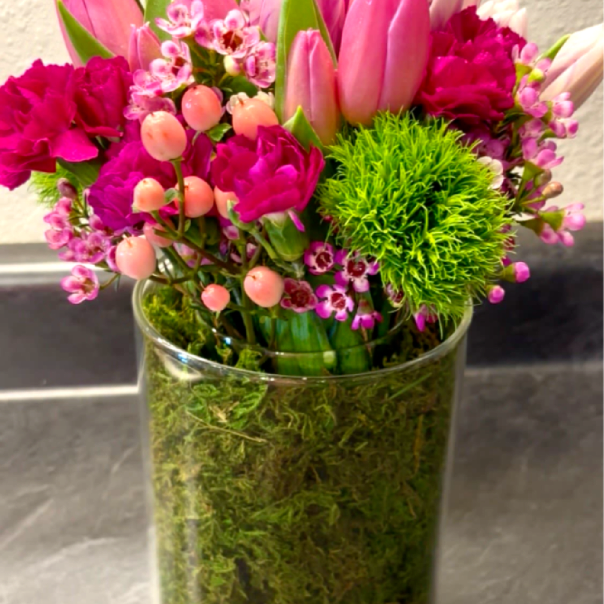 Pink tulips and magenta flowers arranged in a clear glass vase