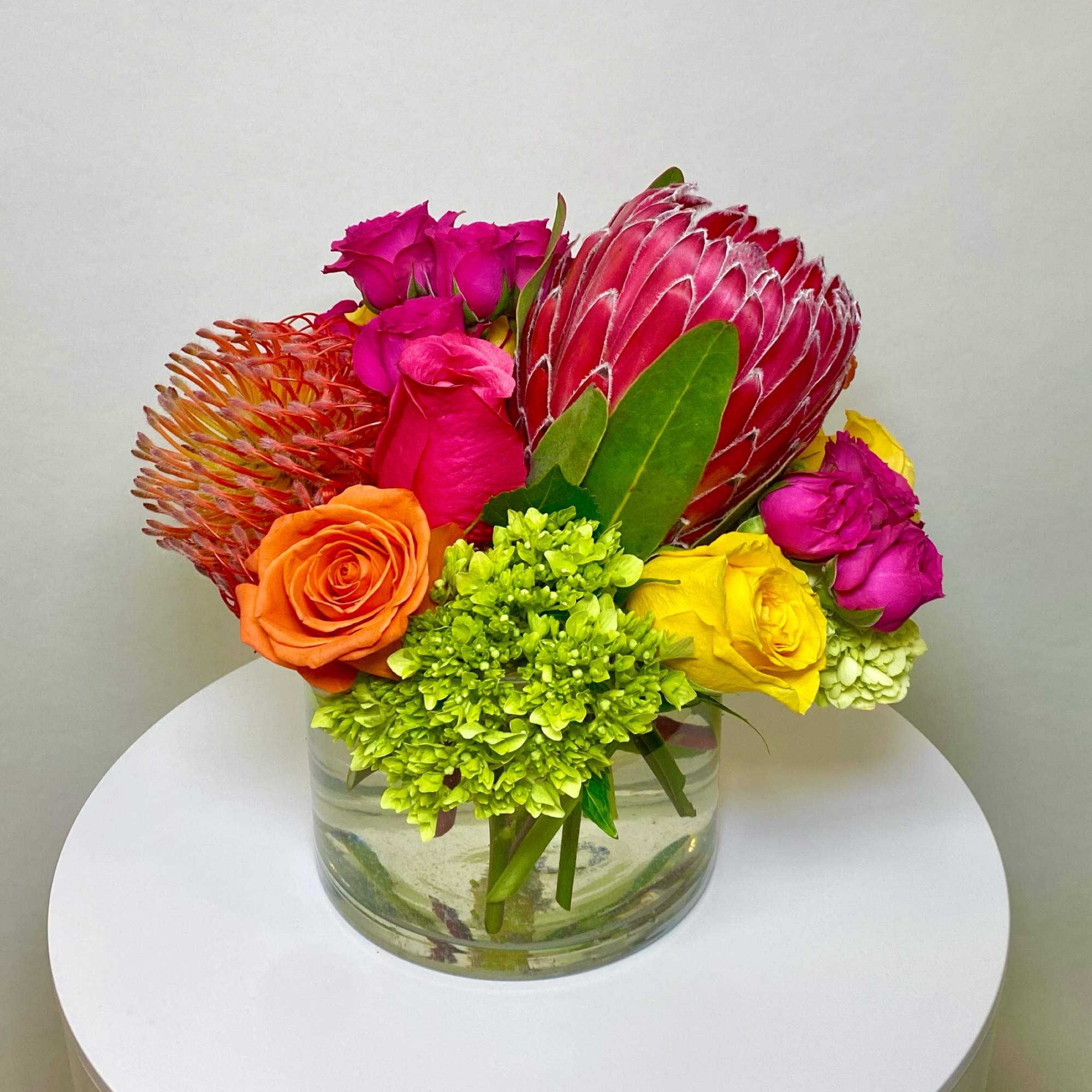 Bright mixed bouquet with roses and a large pink protea in a glass vase
