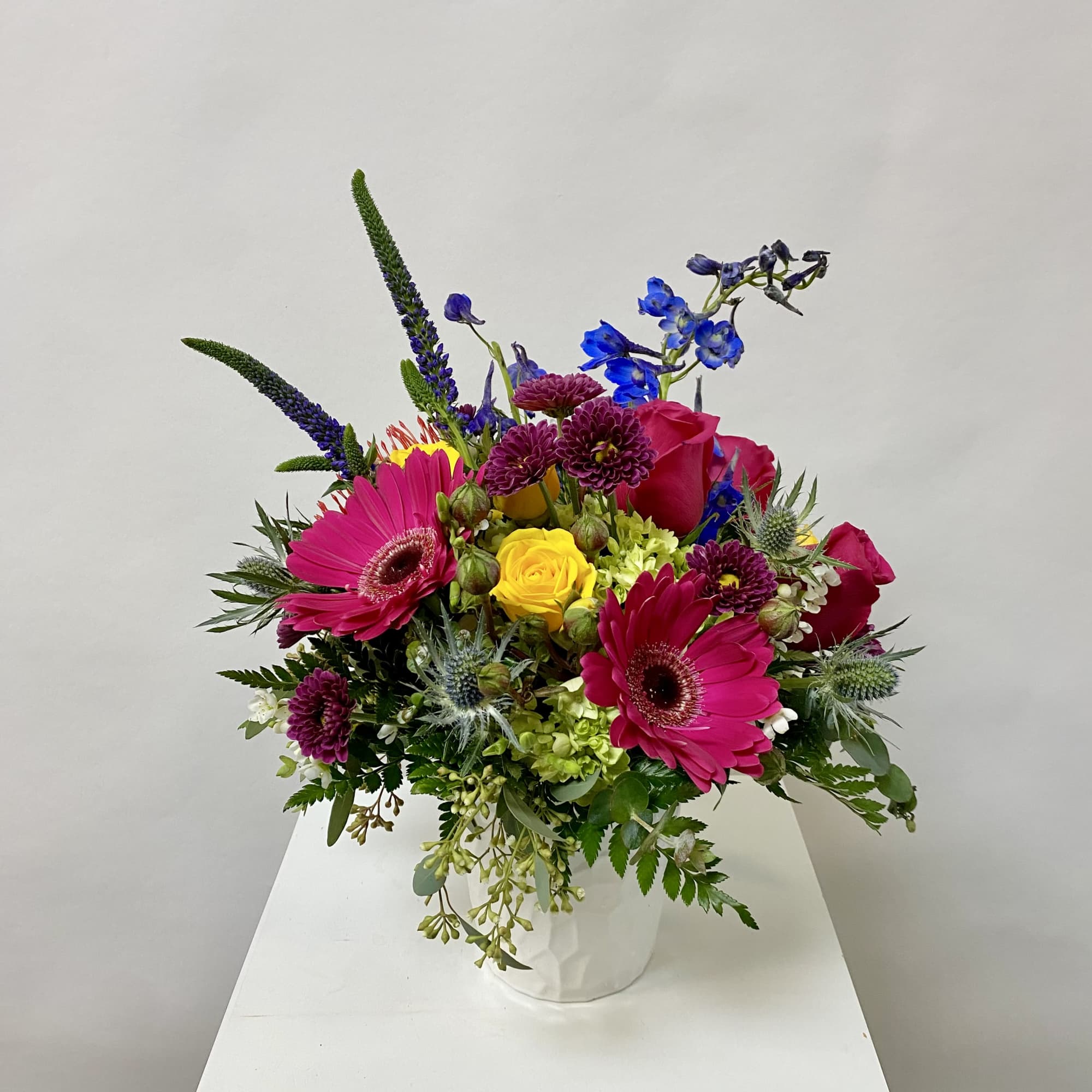 Bright mixed bouquet in a white vase with pink, yellow, and blue flowers
