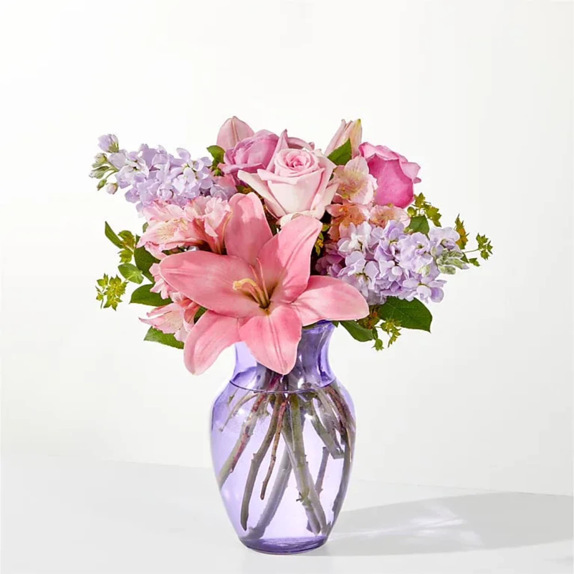 Pink lilies and roses arranged in a purple glass vase