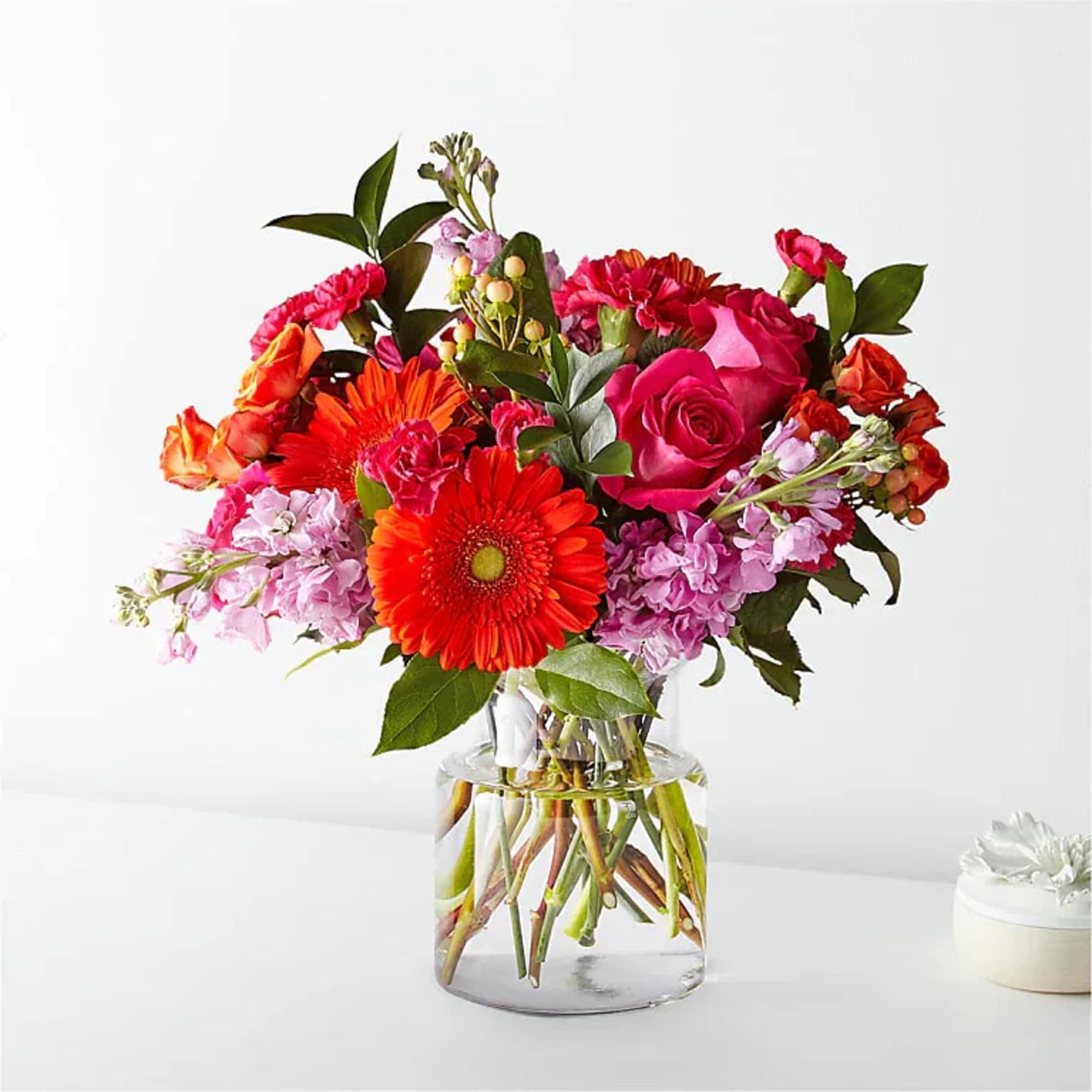 Mixed bouquet of pink, red, and orange flowers in a clear glass vase