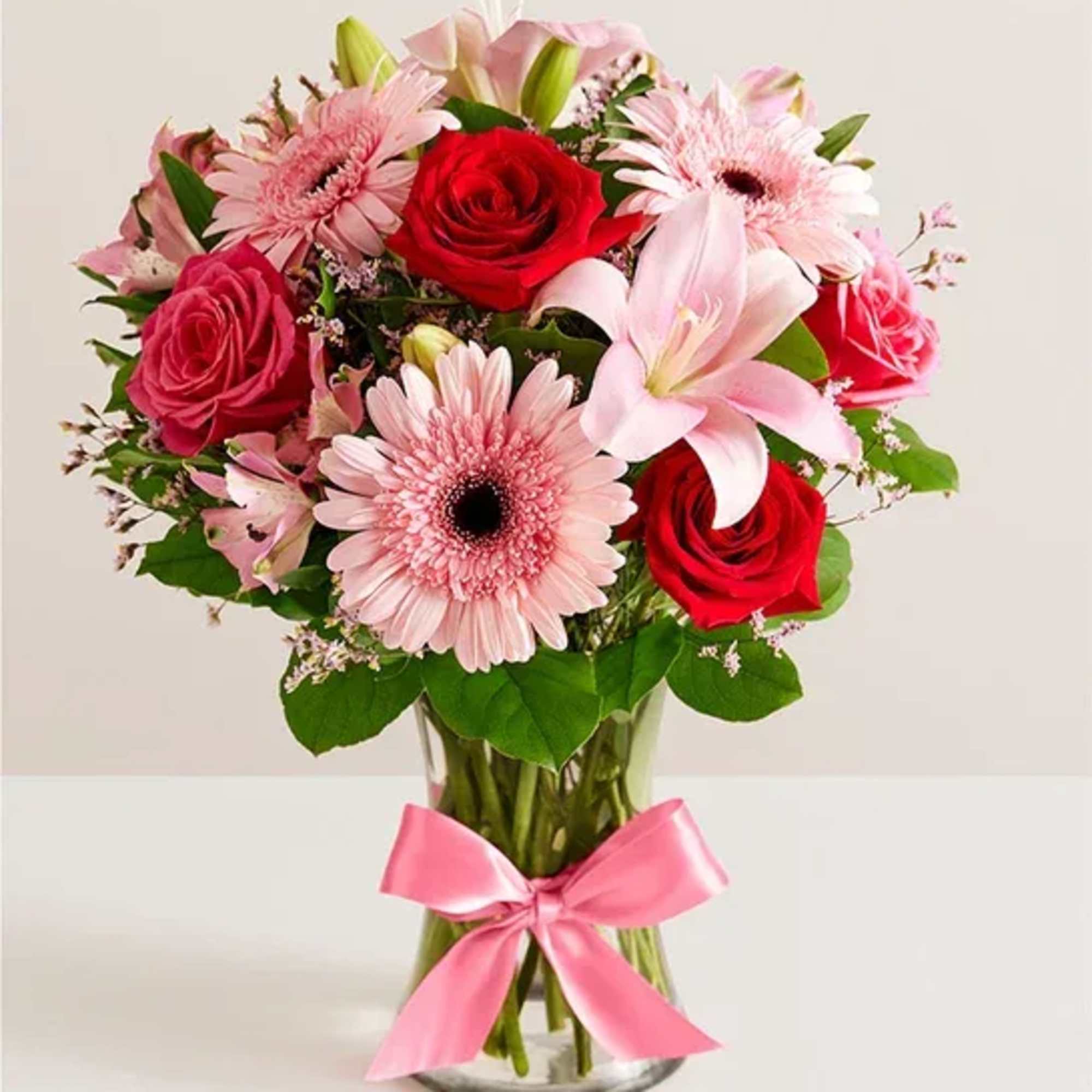 Pink and red flower bouquet in a glass vase with a pink ribbon