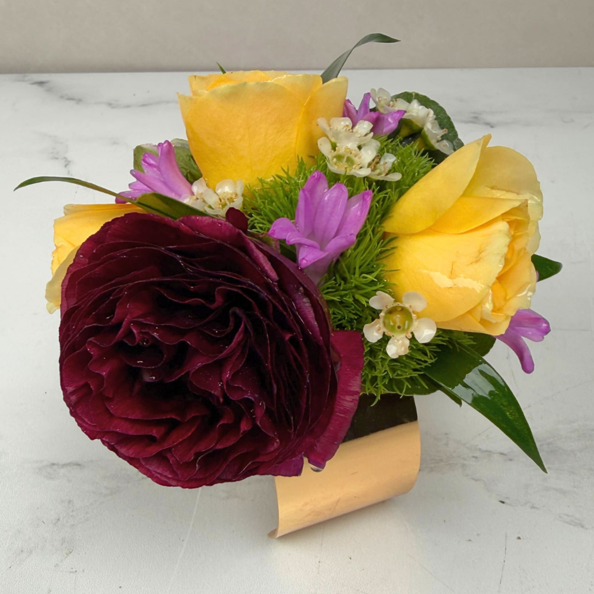 A lush burgundy ranunculus takes center stage in this Velvet Meadow Corsage