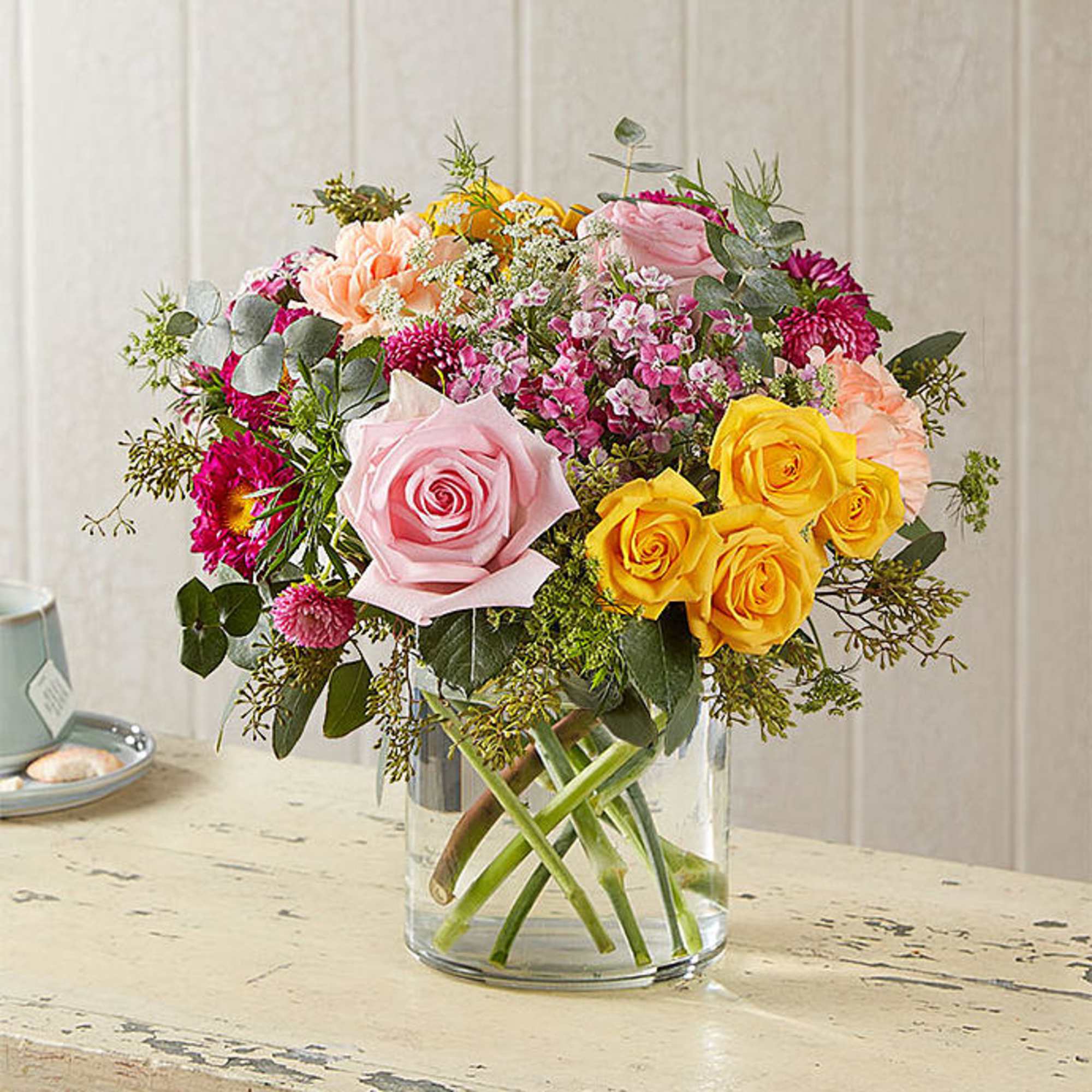 Mixed bouquet of pink, yellow, and peach flowers in a clear glass vase