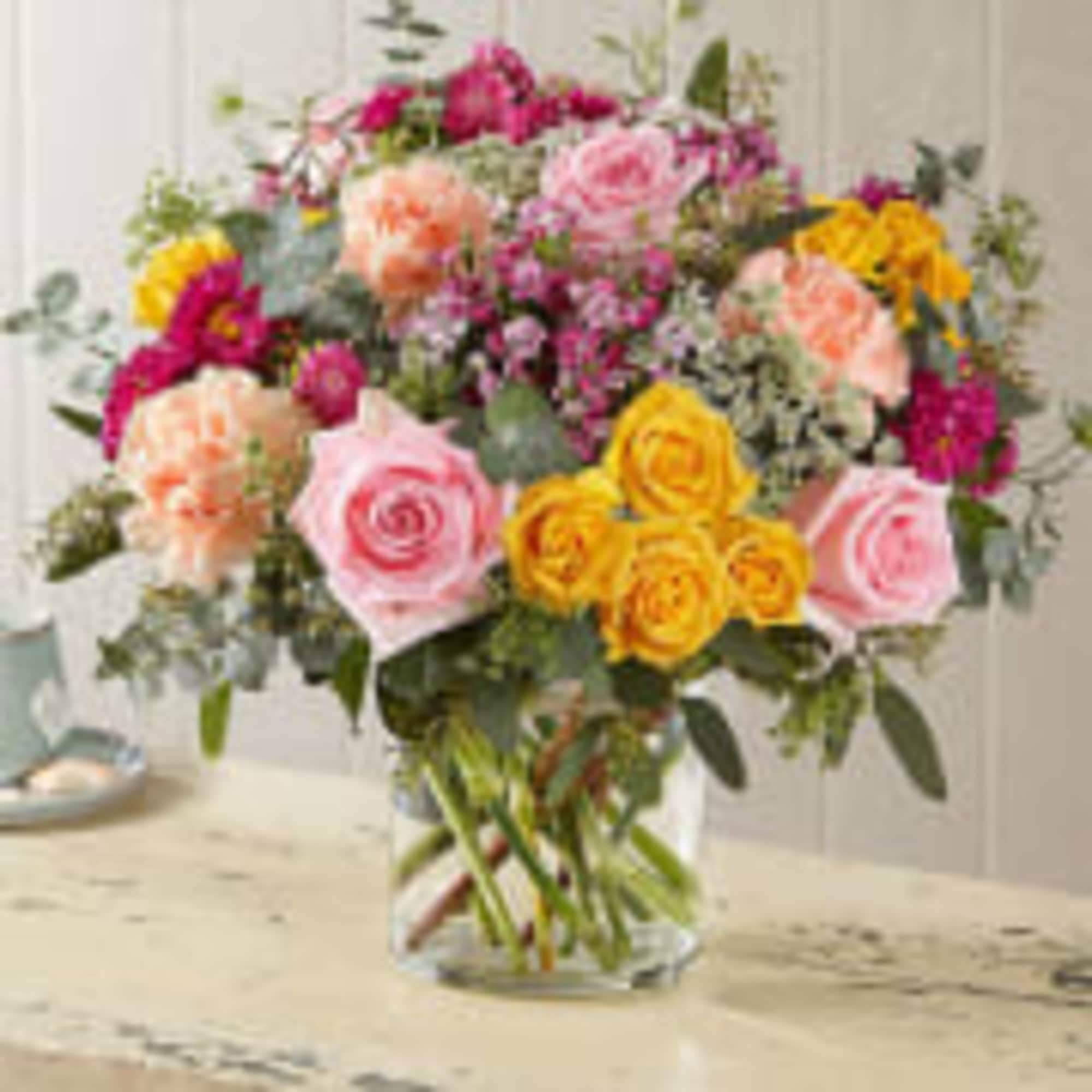 Mixed bouquet of pink, yellow, and peach flowers in a clear glass vase