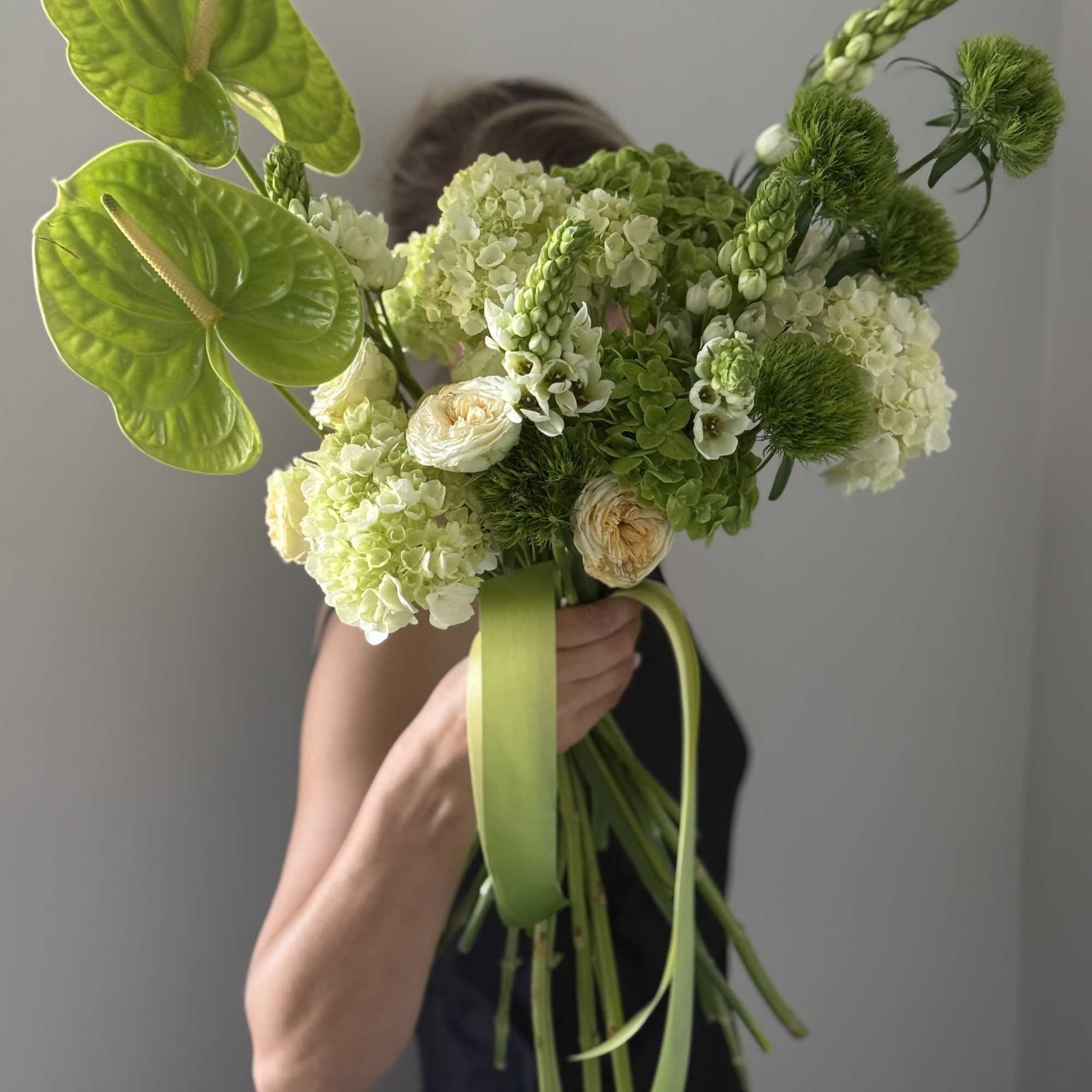 Handheld bouquet with green anthuriums, hydrangeas, and ribbon