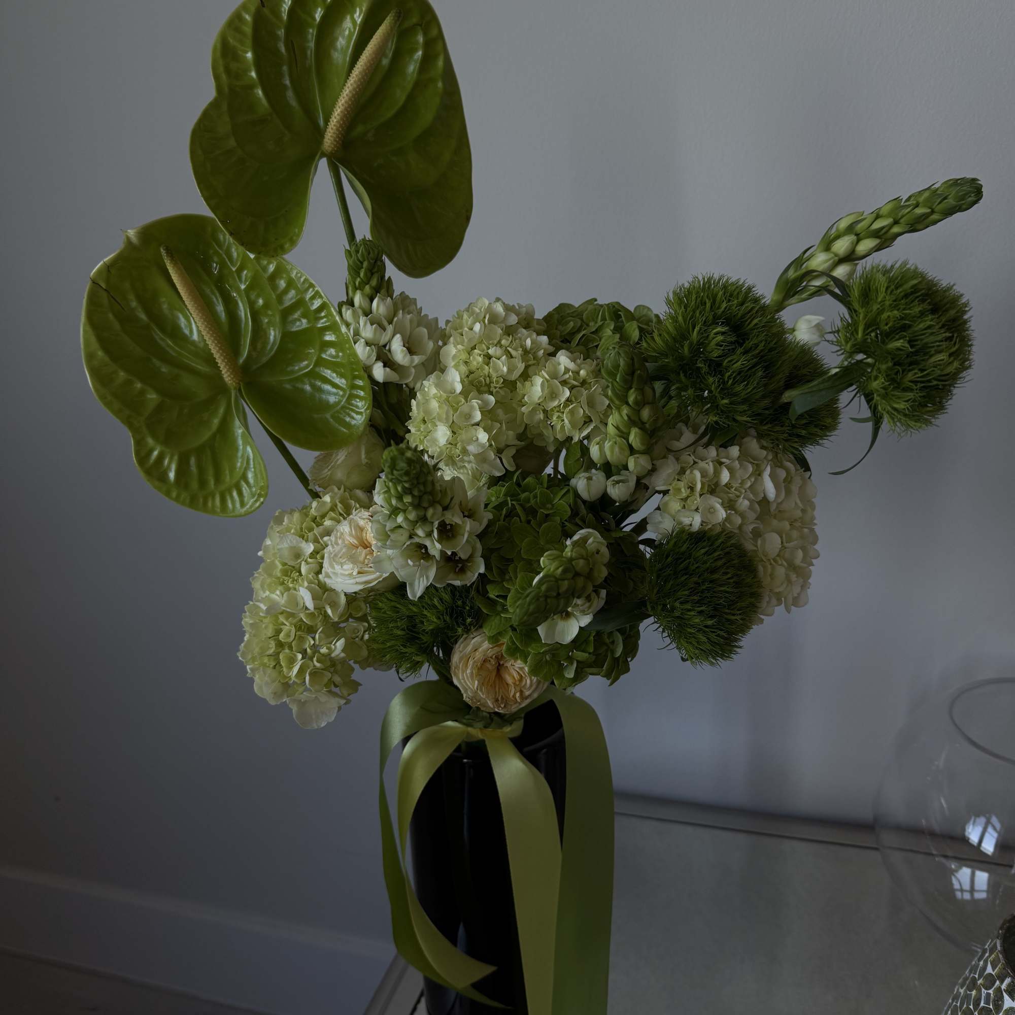 Green floral arrangement with anthuriums and hydrangeas in a black vase