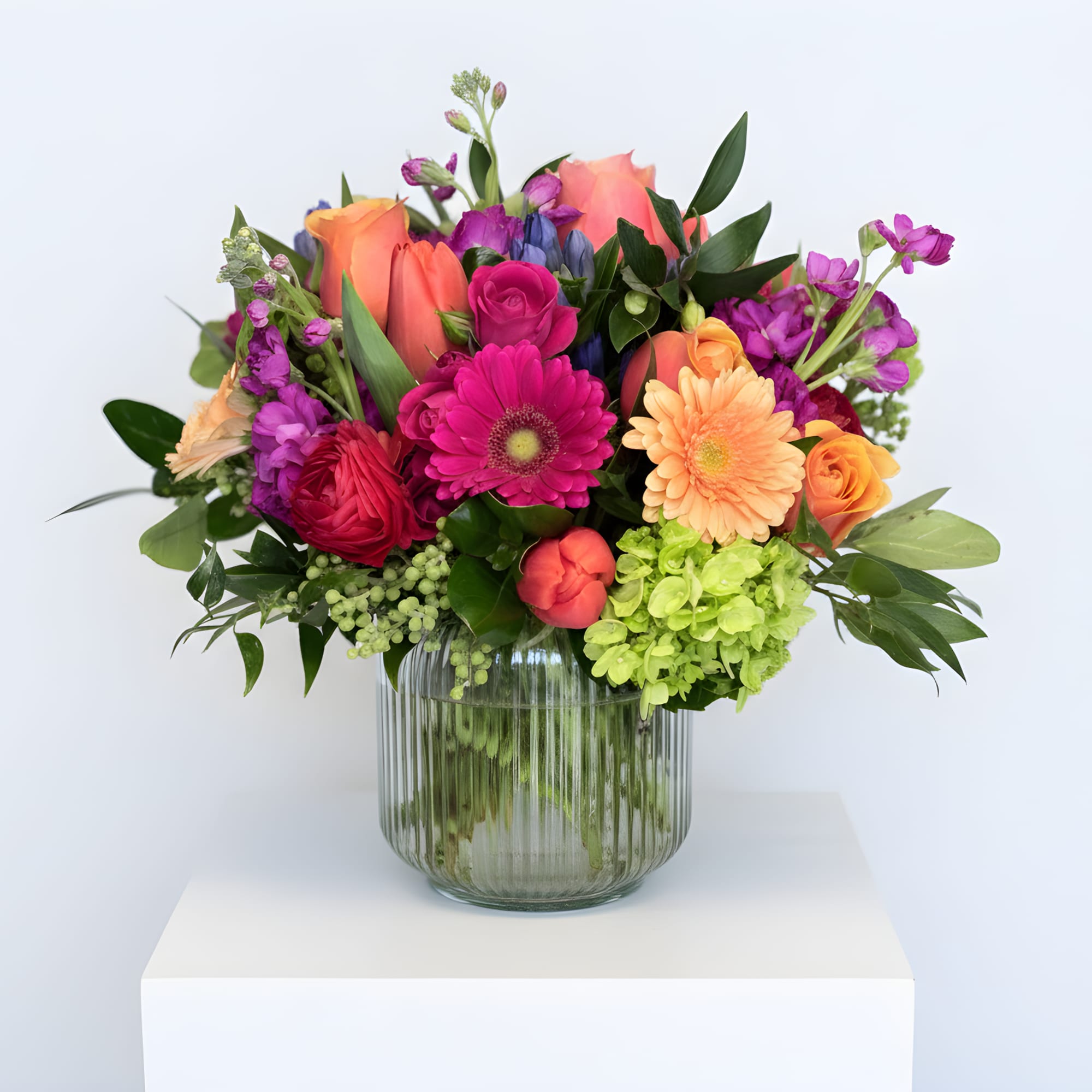 Bright mixed arrangement of pink and orange flowers with green hydrangea in a ribbed glass vase