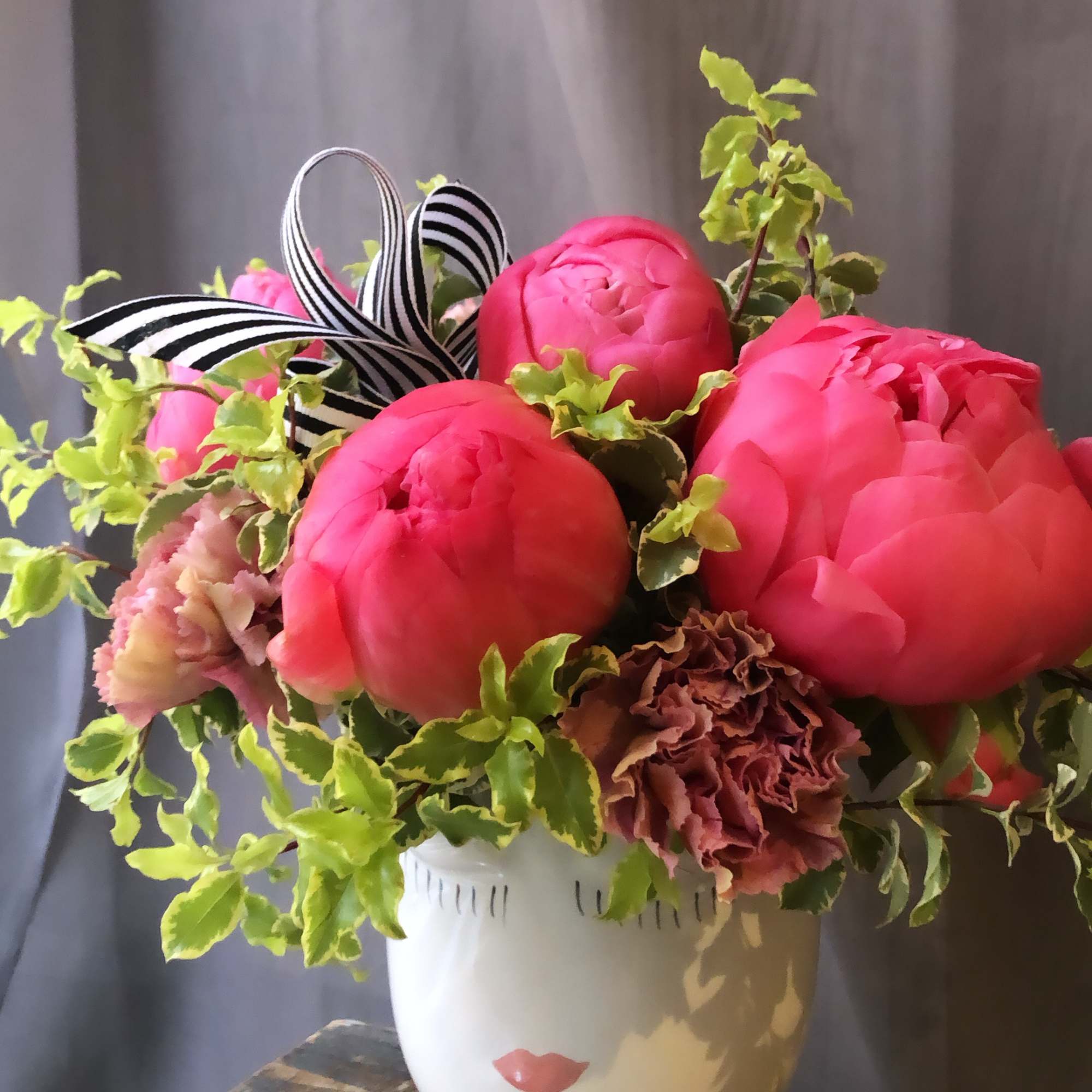 Pink peonies and carnations in a white pedestal vase with striped ribbon