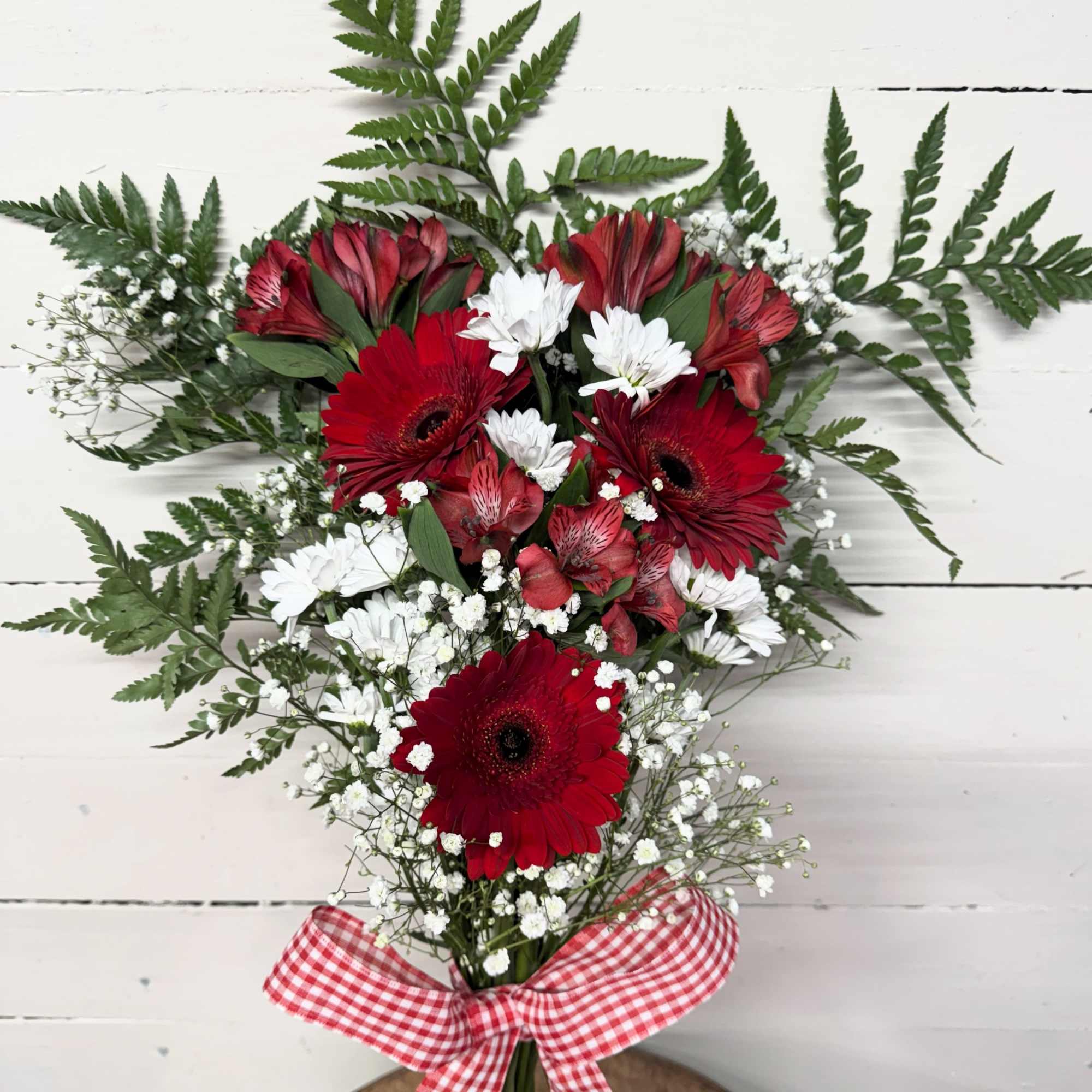 Red gerbera daisies and white filler flowers arranged with a gingham bow.