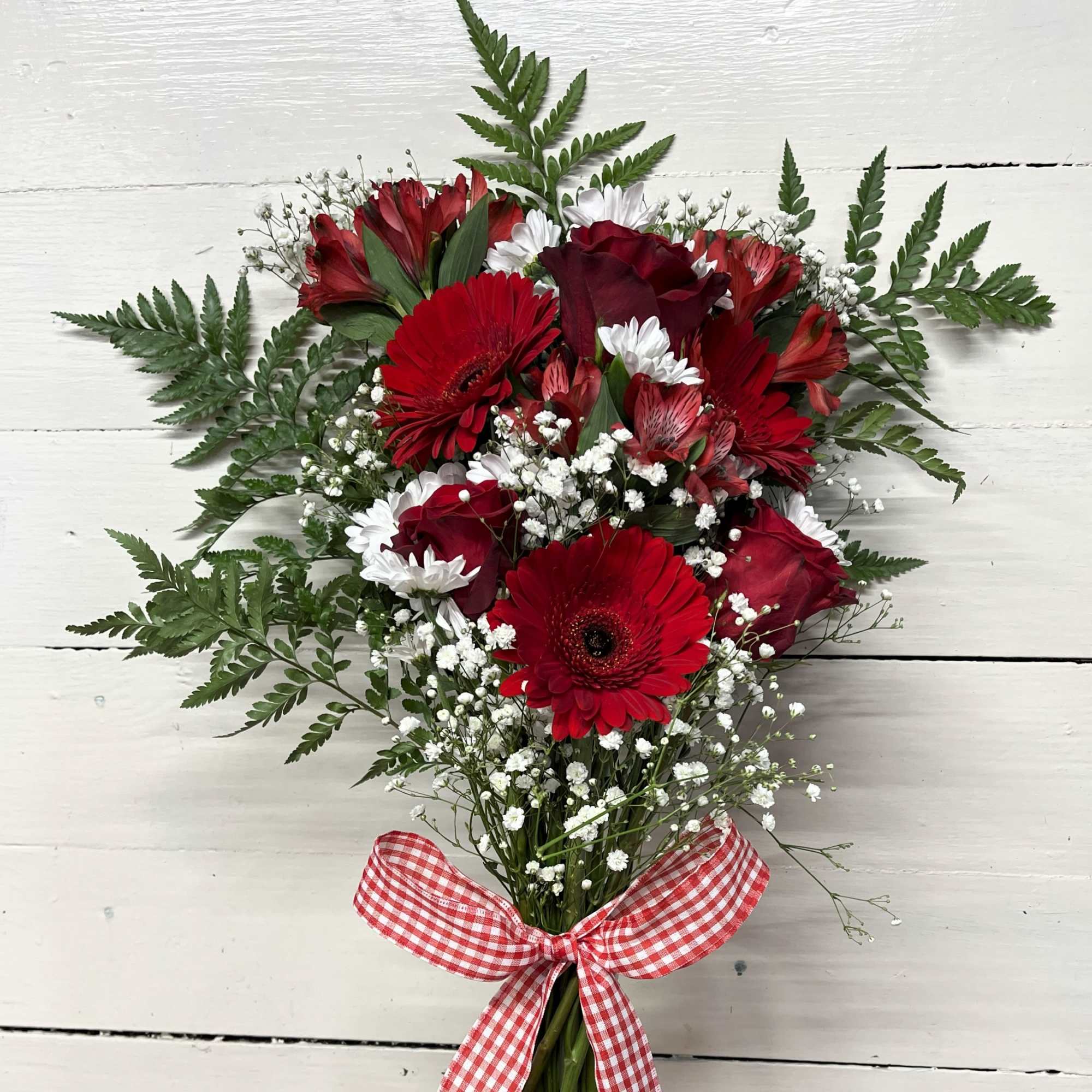 Red and white bouquet with daisies, roses, and baby's breath tied with a gingham ribbon