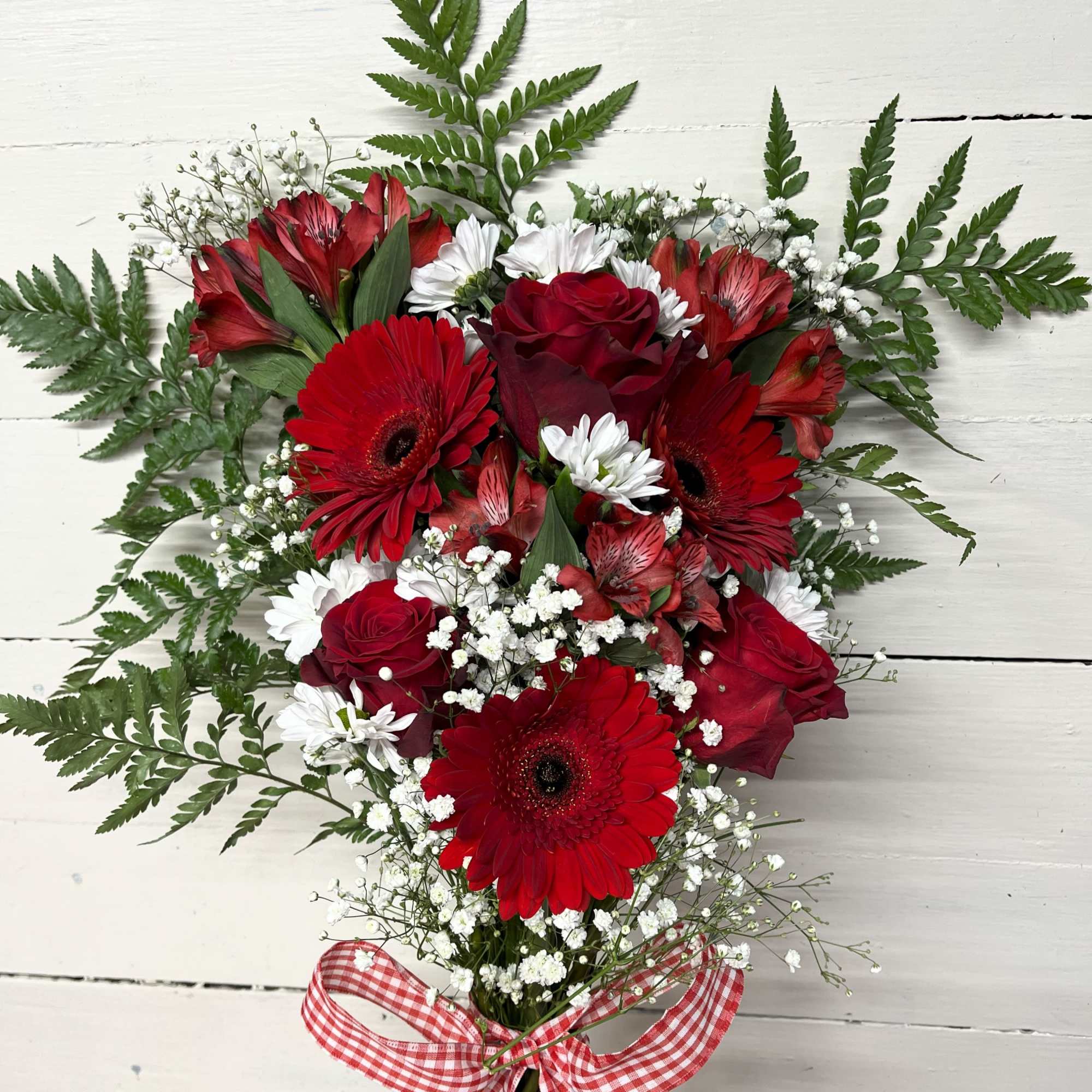 Red roses and gerbera daisies with white filler flowers and a gingham ribbon