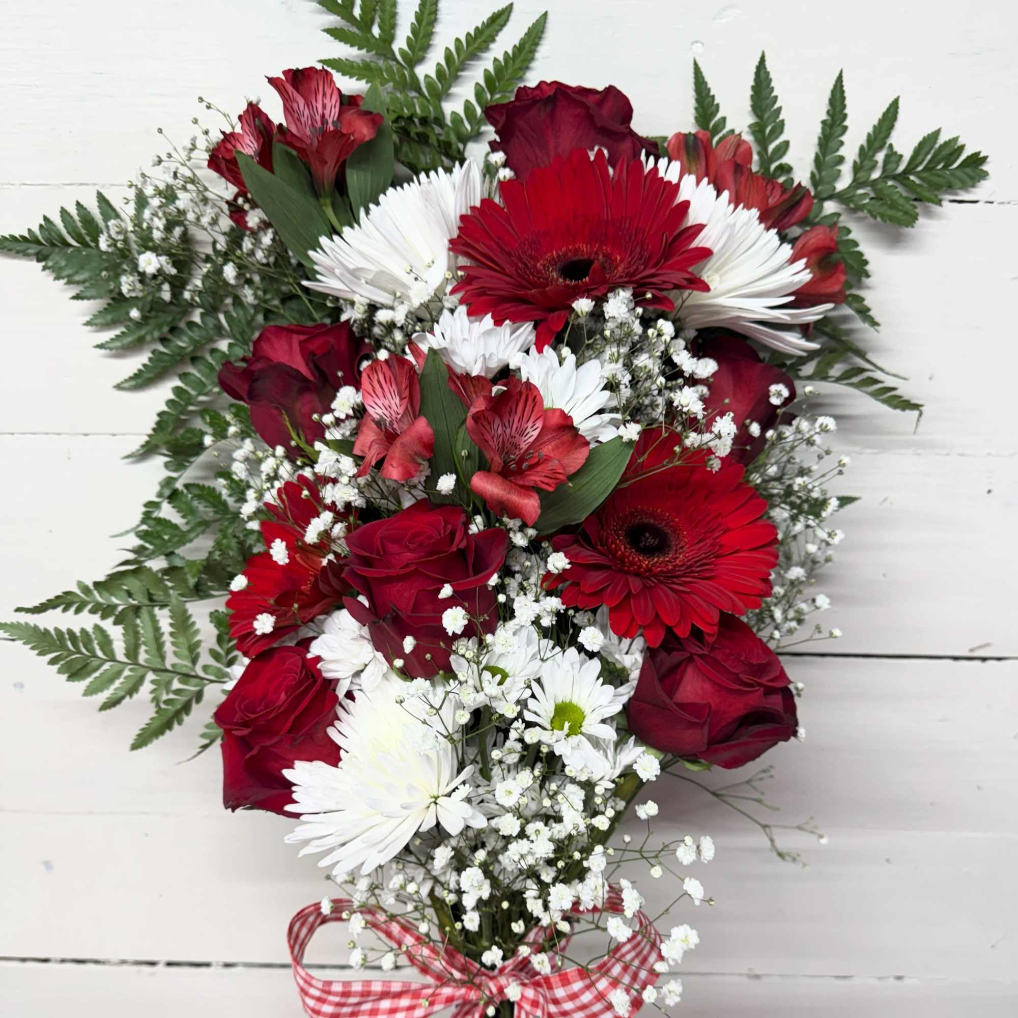 Red roses and white daisies arranged with baby's breath and fern foliage.