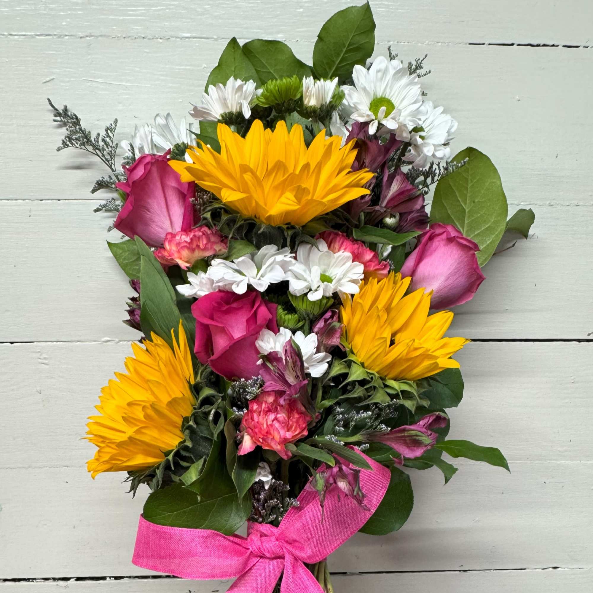 Bouquet of yellow sunflowers, pink roses, and white daisies tied with a pink ribbon