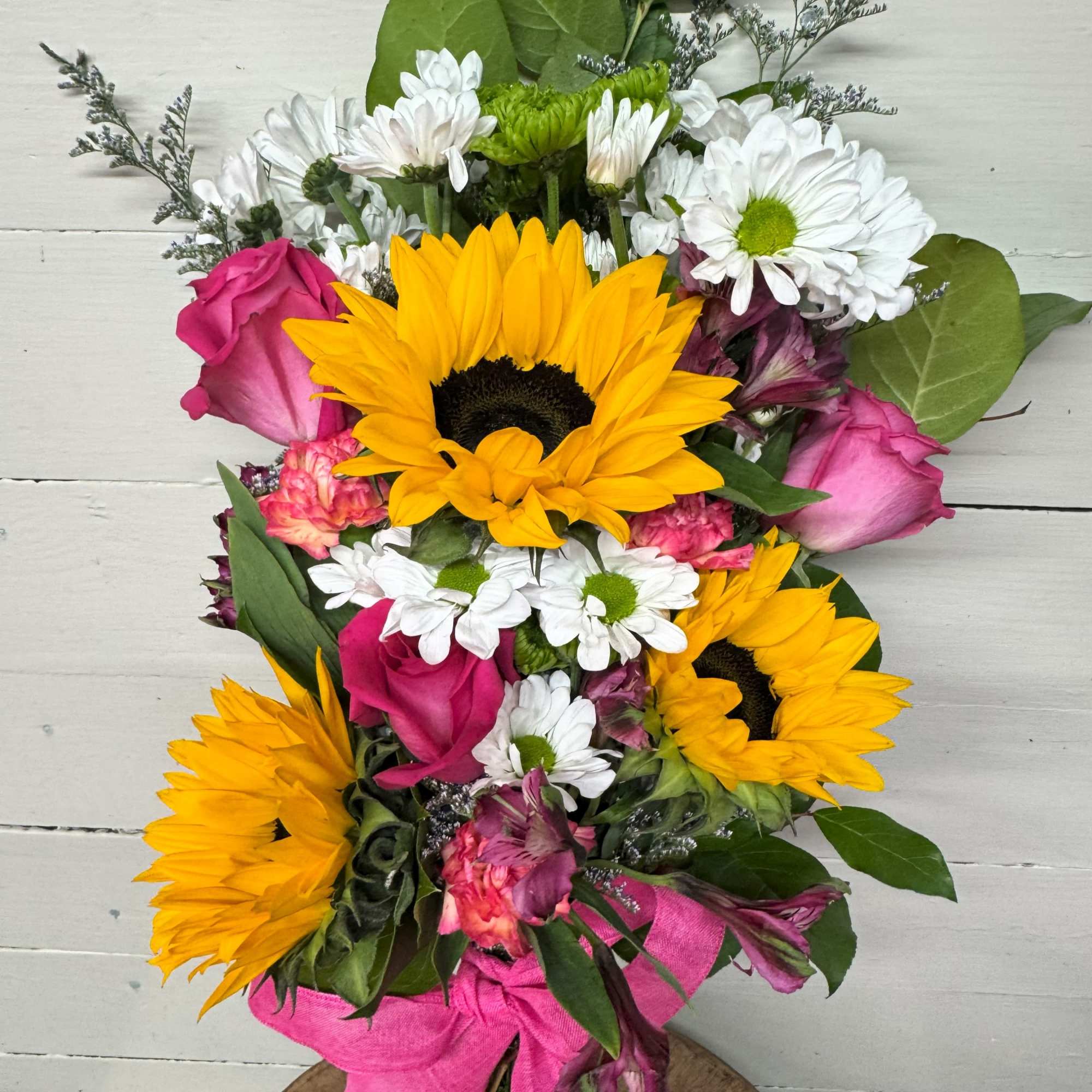Bouquet of sunflowers, pink roses, and white daisies with a pink wrap
