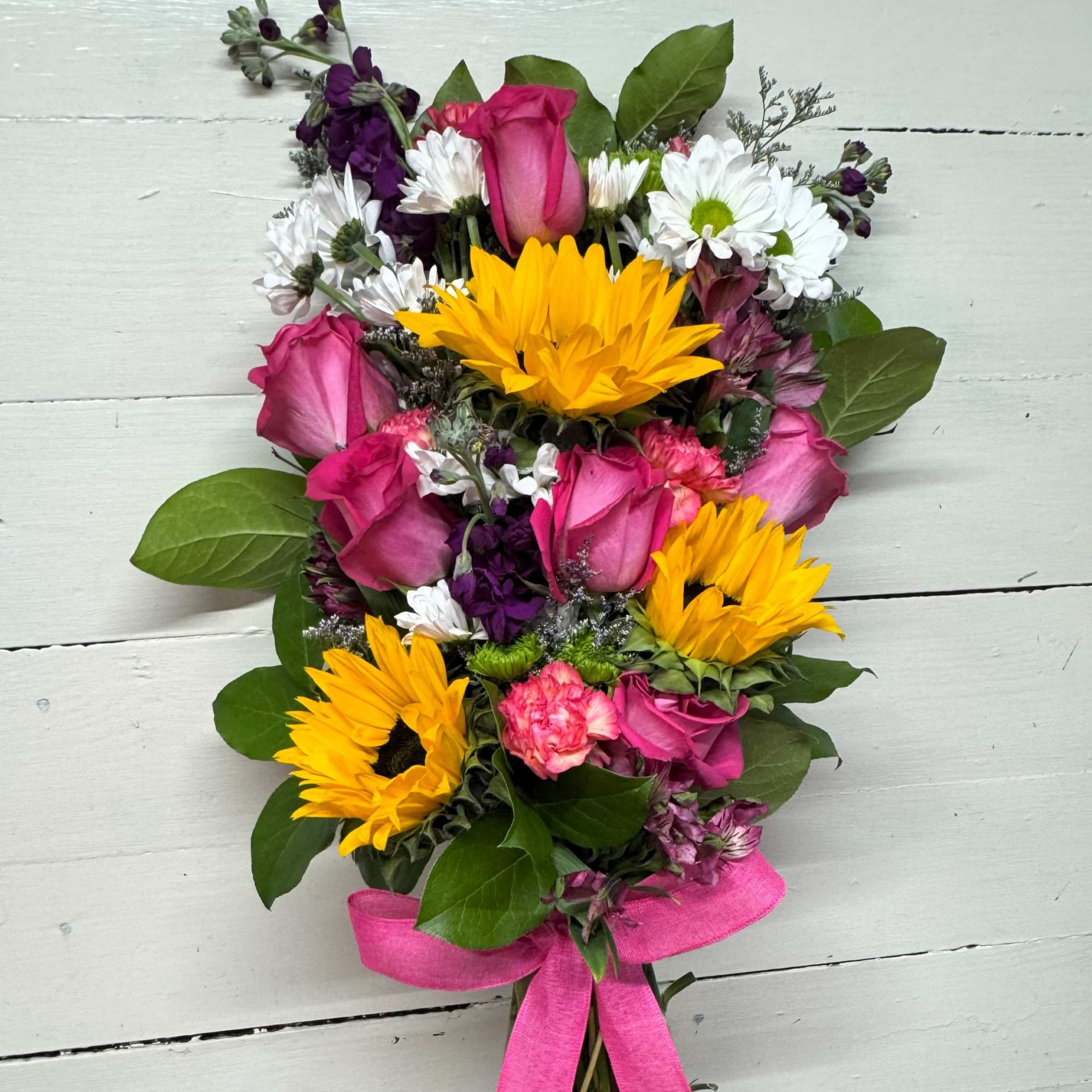 Bouquet of pink roses, yellow sunflowers, and white daisies tied with a pink ribbon