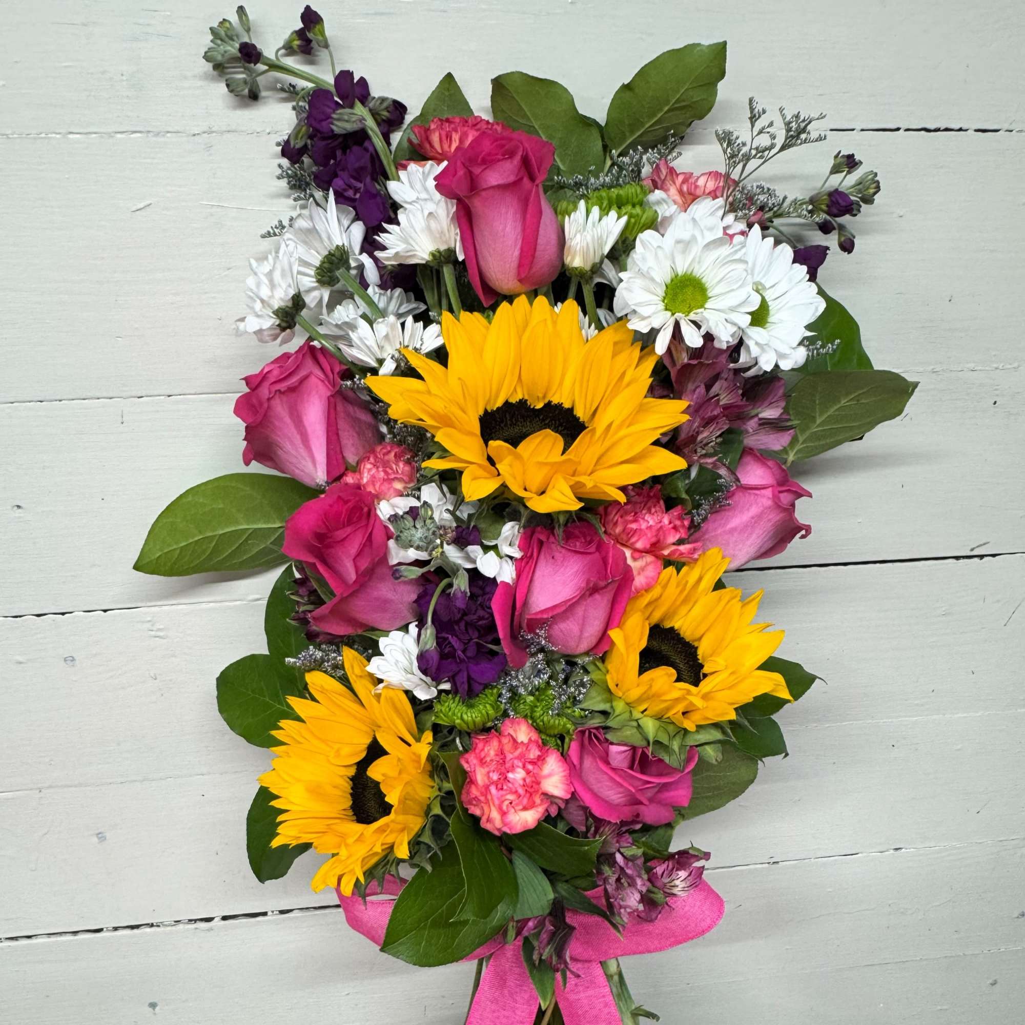 Bouquet of sunflowers, pink roses, white daisies, and purple flowers tied with a pink ribbon