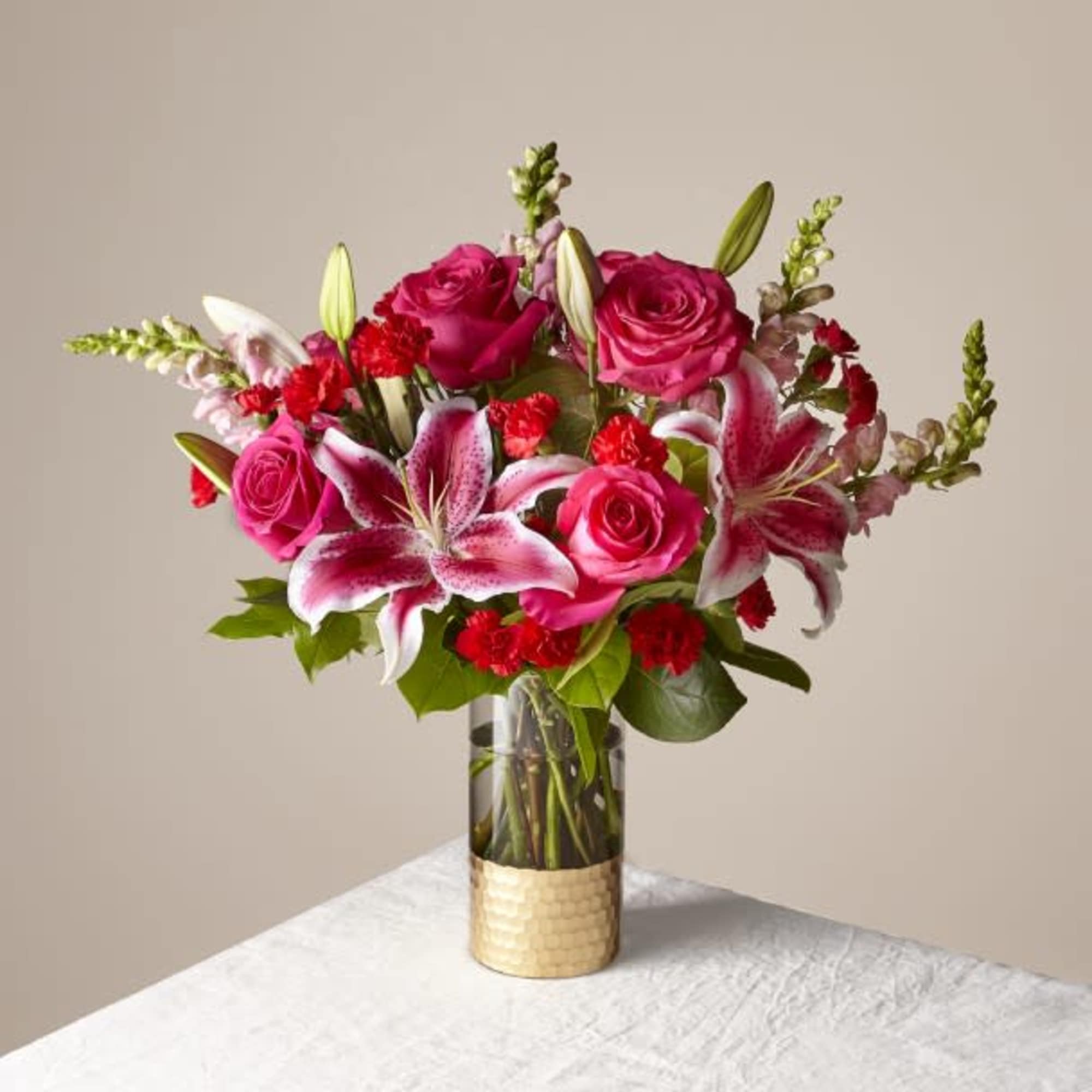 Pink roses and lilies arranged in a clear vase with a gold wrap