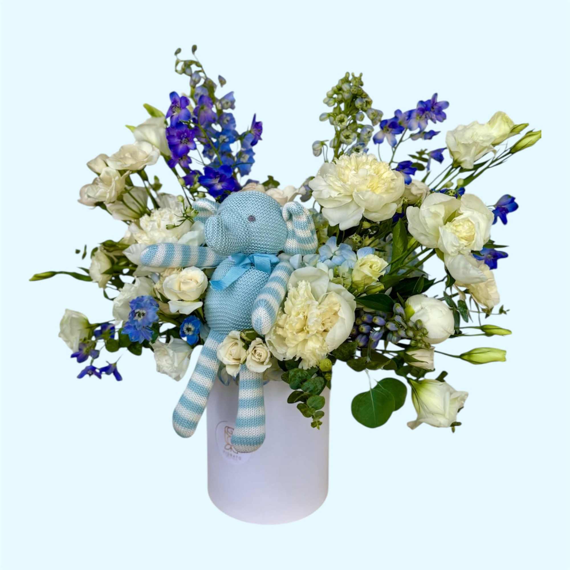 White and blue flower arrangement in a round box with a knitted teddy bear