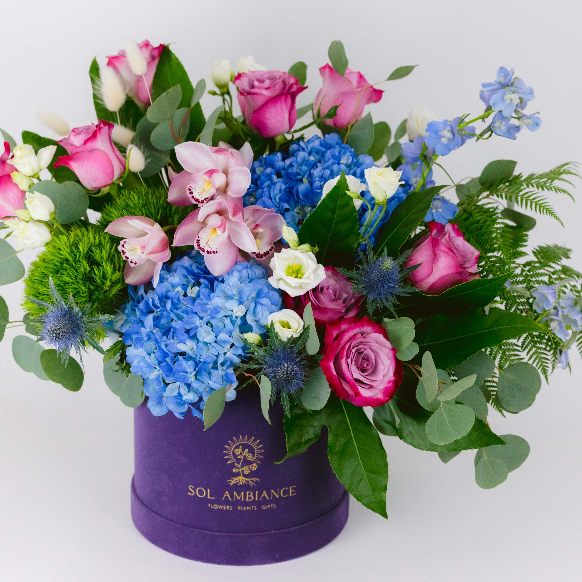 Mixed bouquet in a purple hat box with pink, blue, and white flowers
