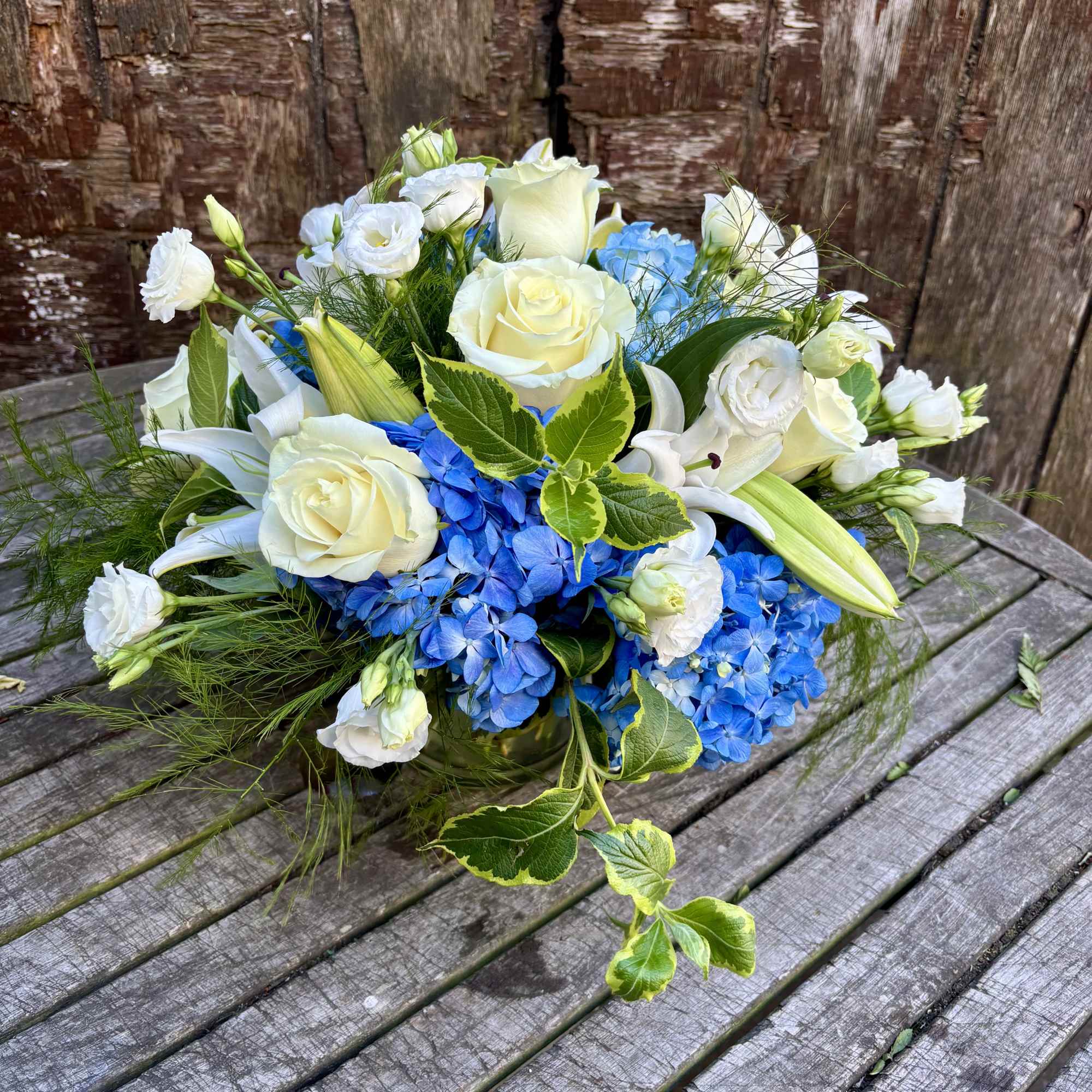 Bouquet of white roses, blue hydrangeas, and white lilies on a wooden table