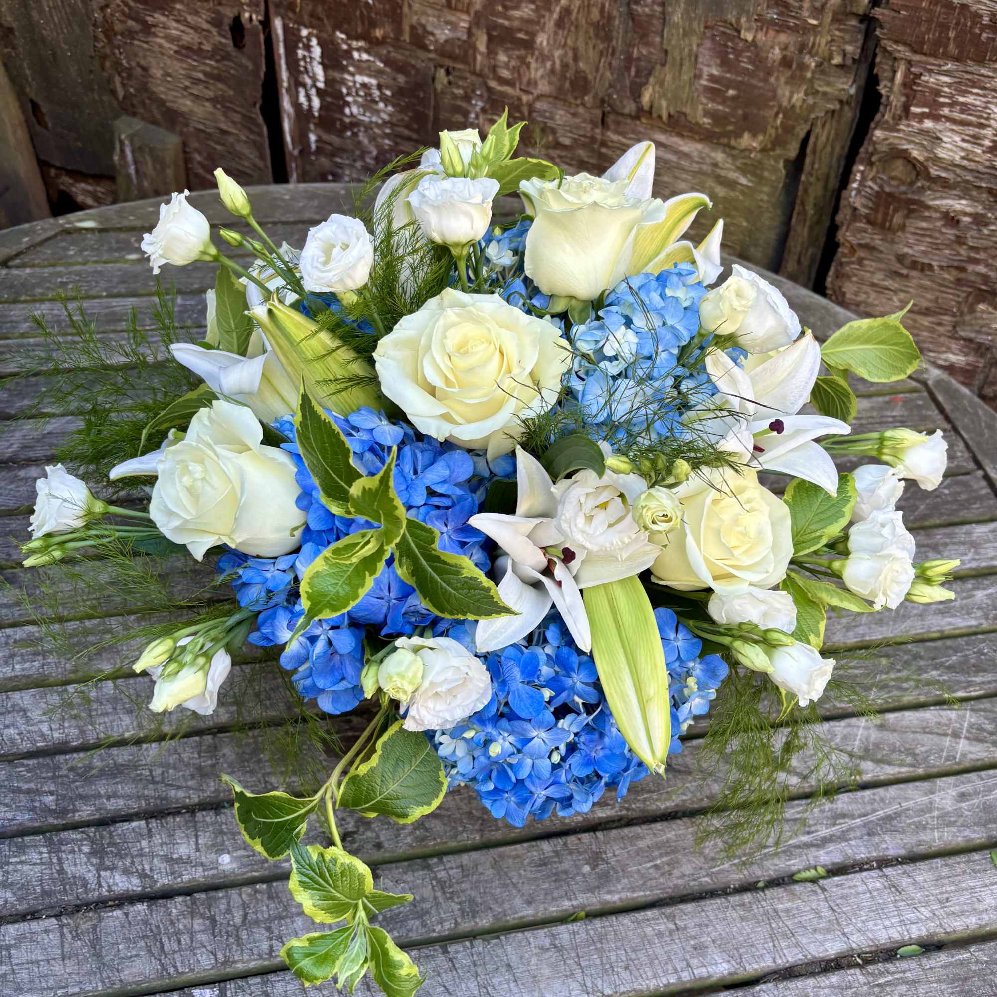 White roses and lilies with bright blue hydrangeas in a low bouquet.