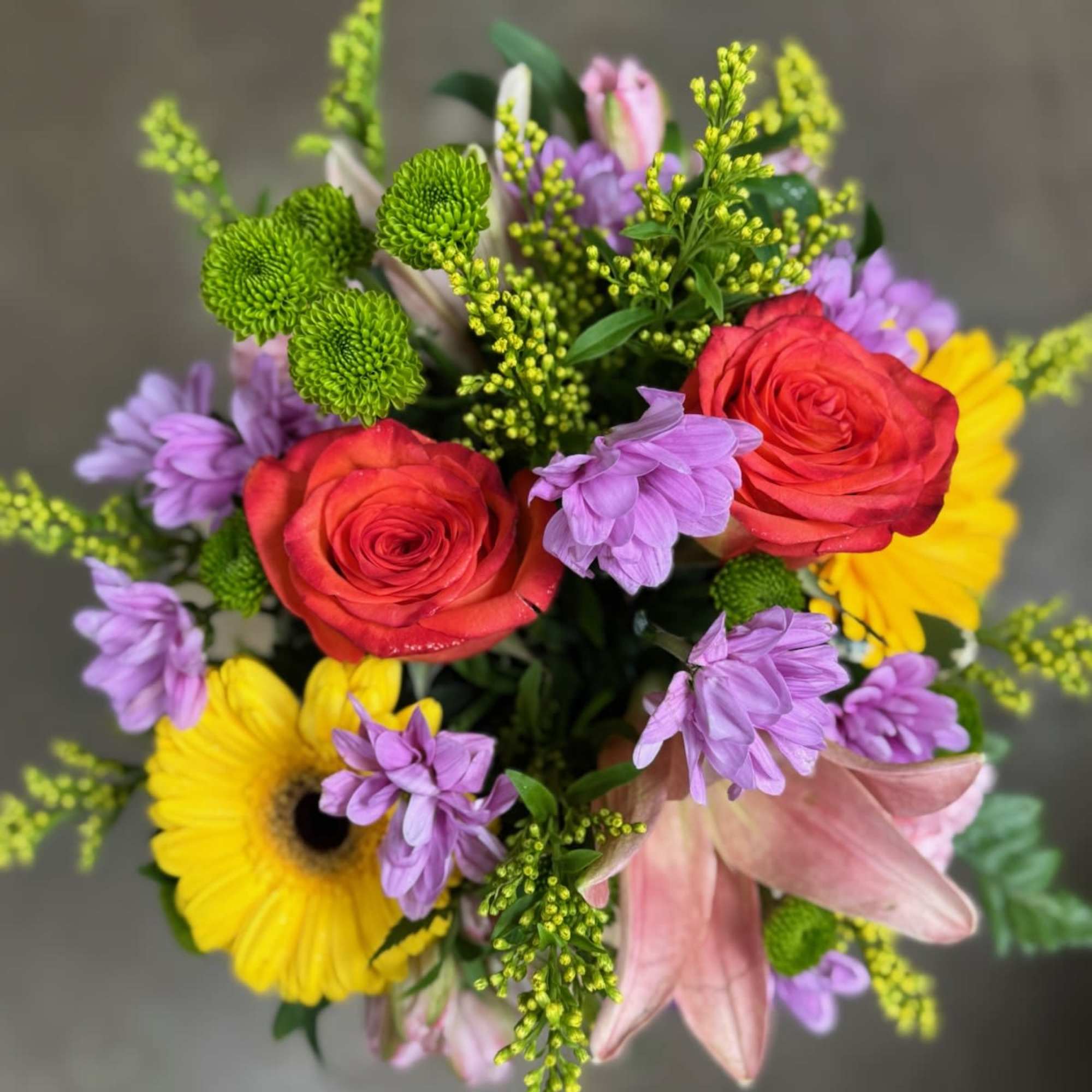 Bouquet of red roses, yellow gerbera daisies, and purple flowers