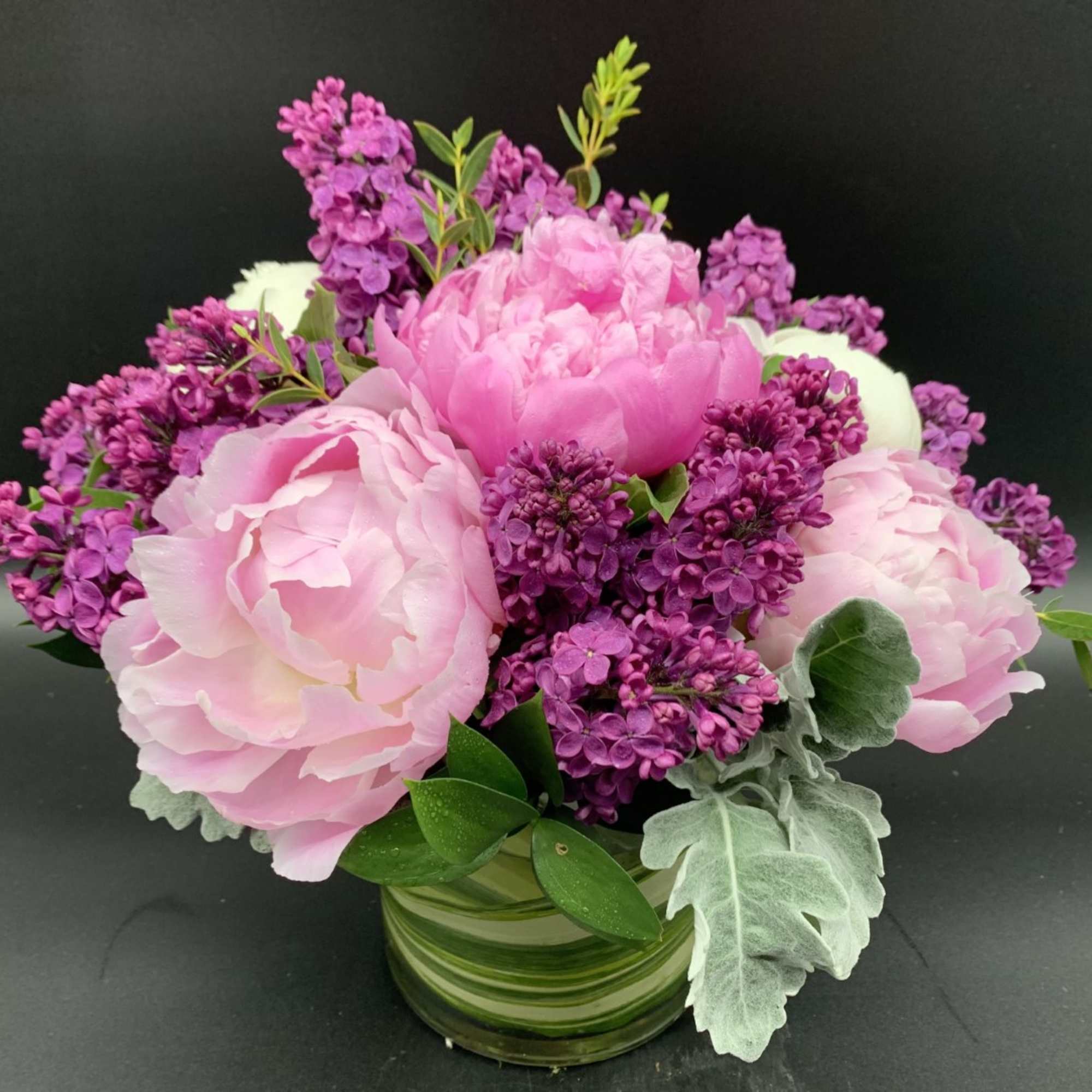 Pink peonies and purple lilacs in a striped glass vase