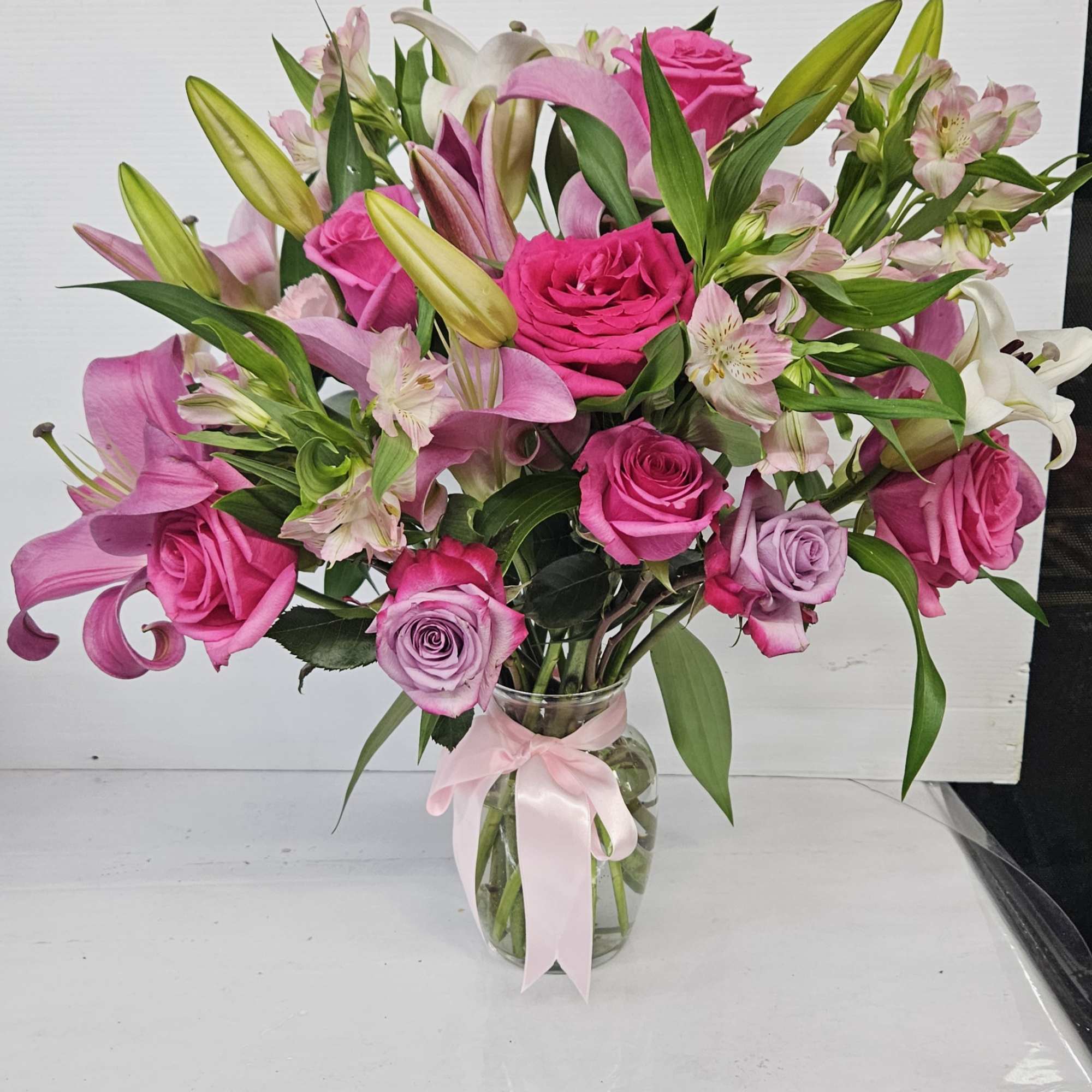Pink roses and lilies arranged in a glass vase with a pink ribbon.