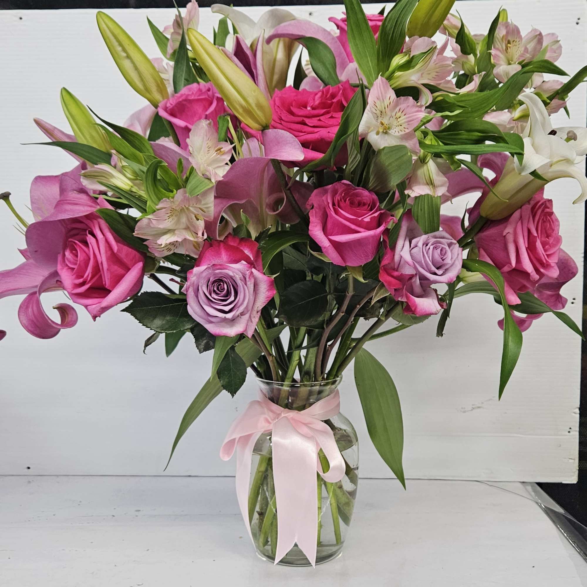 Pink roses and lilies arranged in a clear glass vase with a pink ribbon