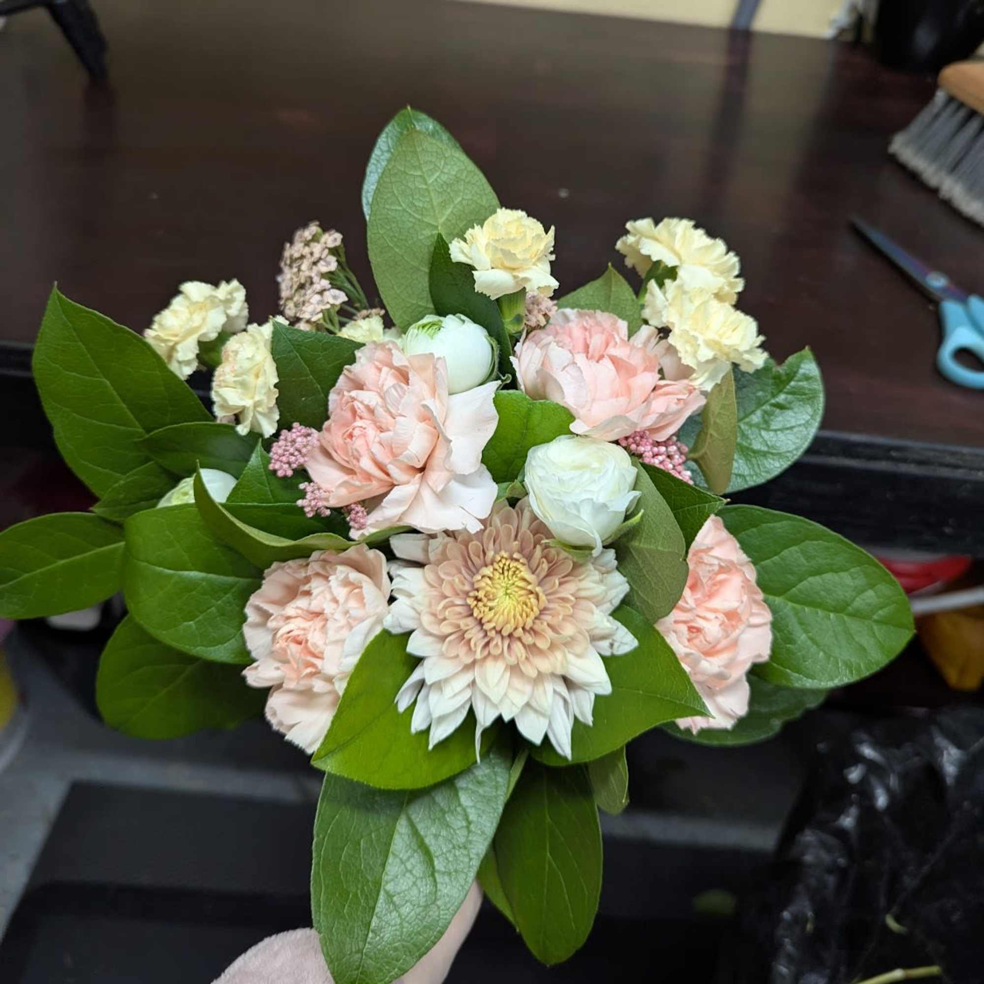 Handheld bouquet of pale pink and cream flowers with large green leaves