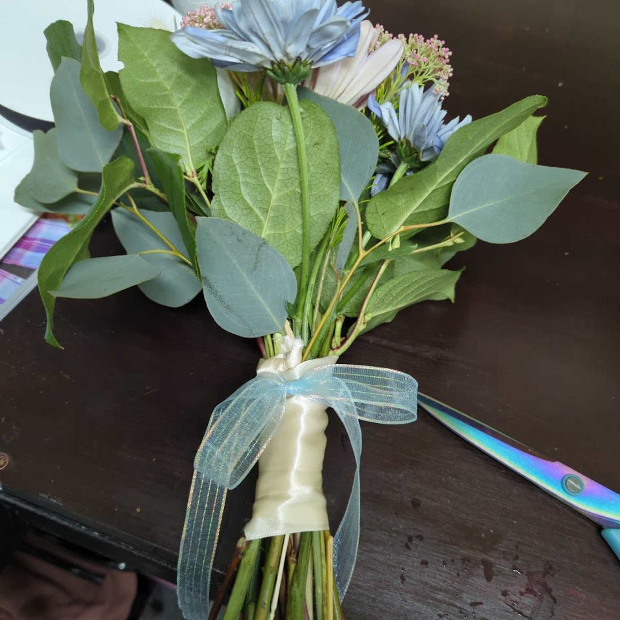 Hand-tied bouquet with blue daisies and greenery tied with a ribbon